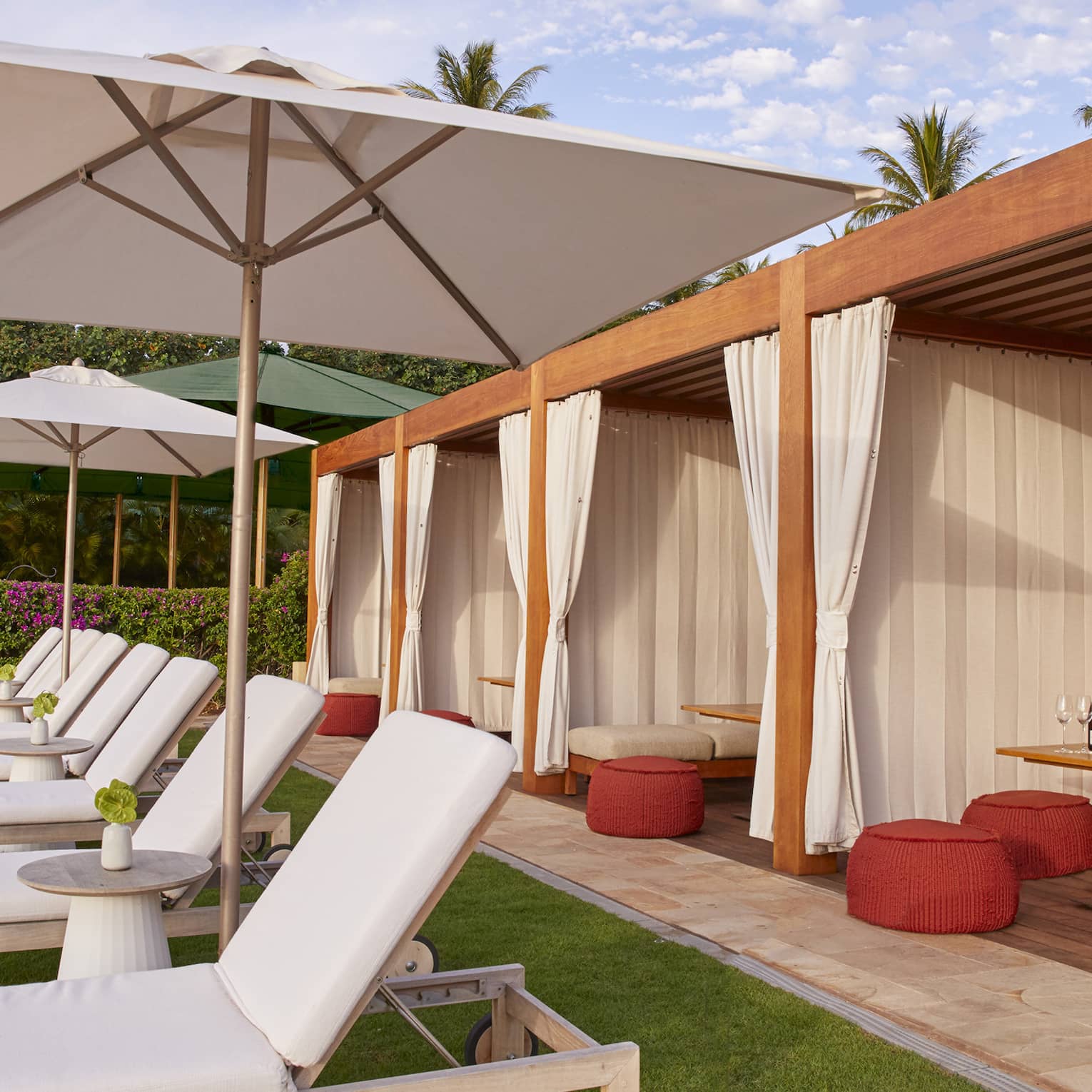 Patio lounge chairs with white cushions in front of three cabanas with curtains