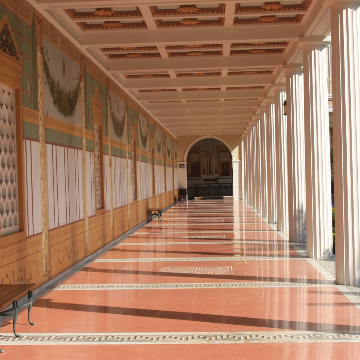 A long hallway with orange floors and columns on the side leading to an arched doorway.