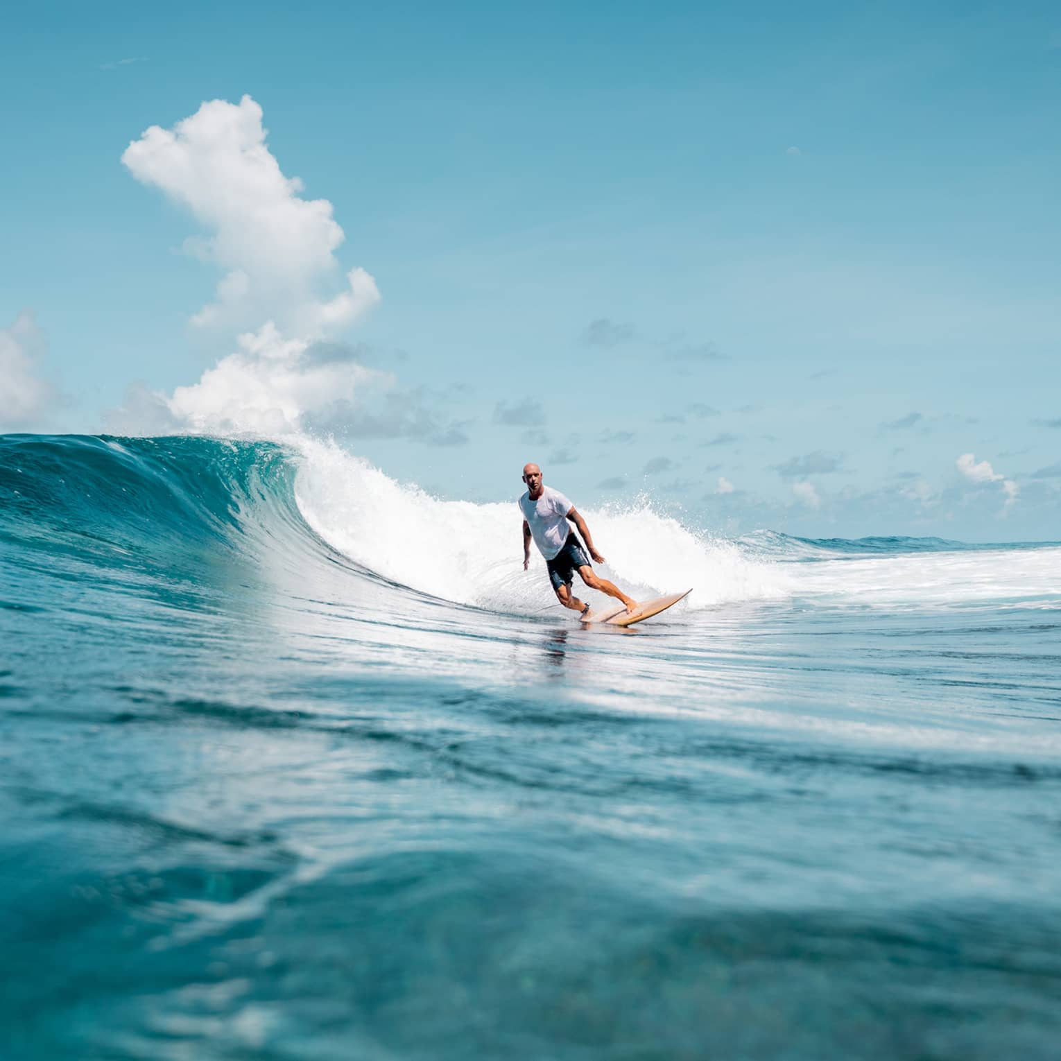 A person surfing a wave in the ocean, the water is a deep blue matched by the blue sky.