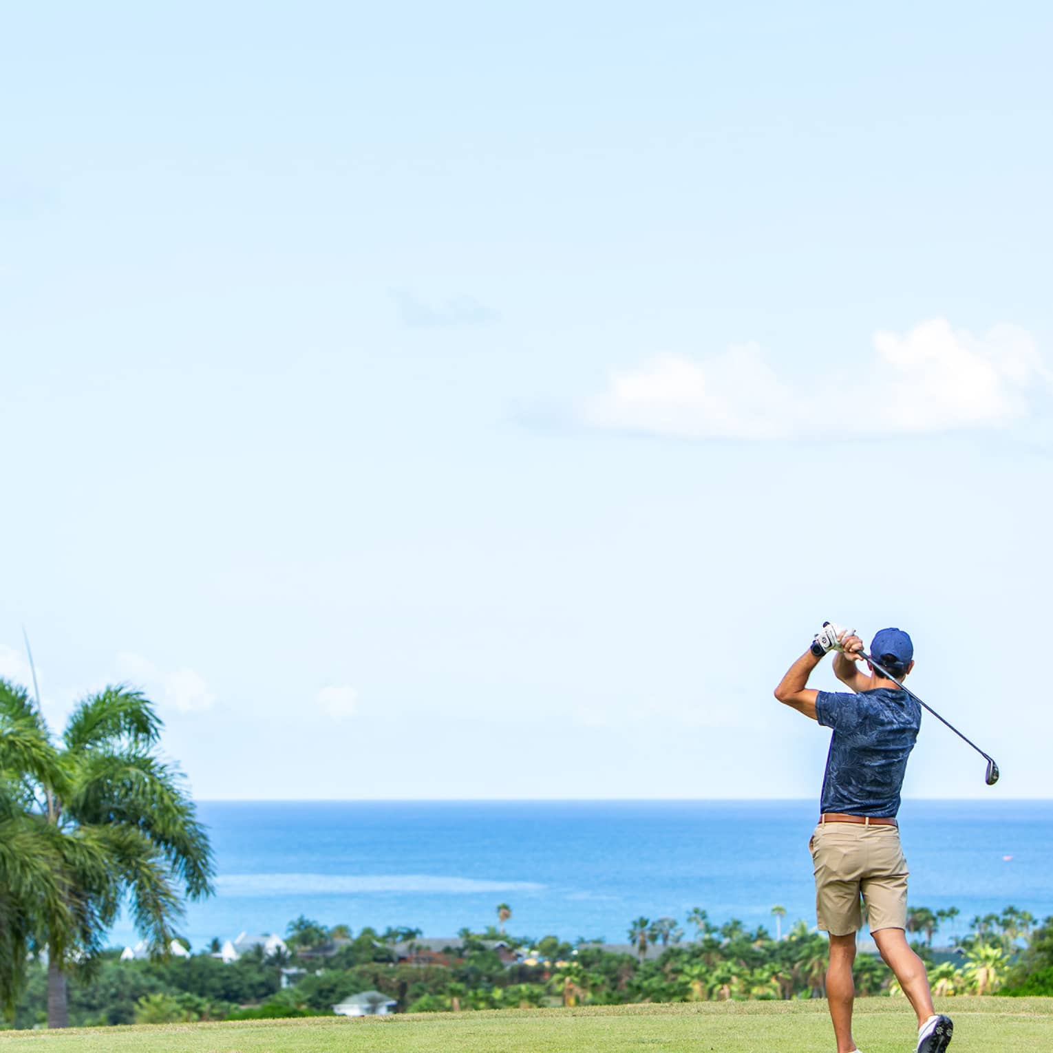 ,A man playing gold near palm trees and and ocean.