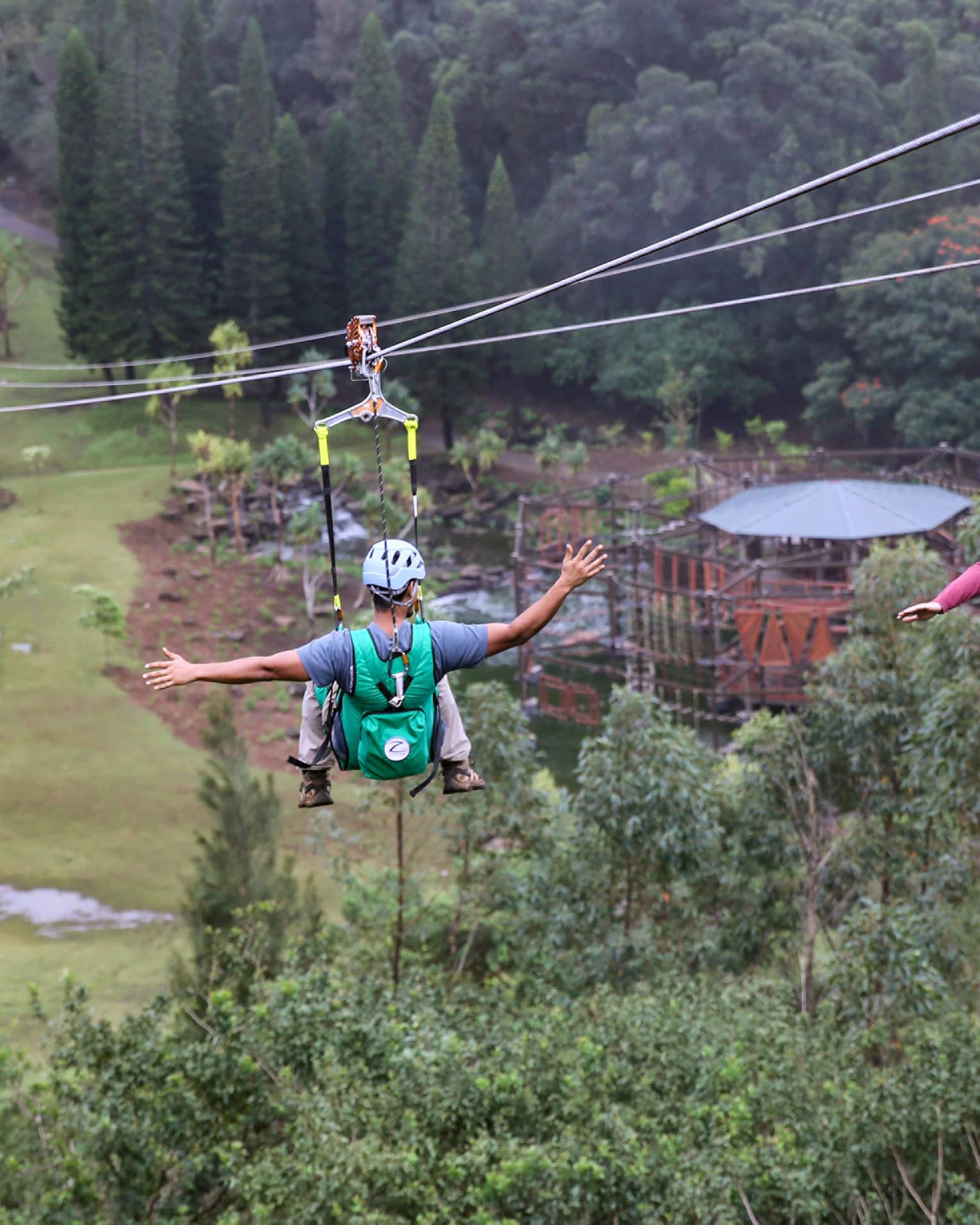 Adventure Park, two people glide down zip lines high above trees over mountain