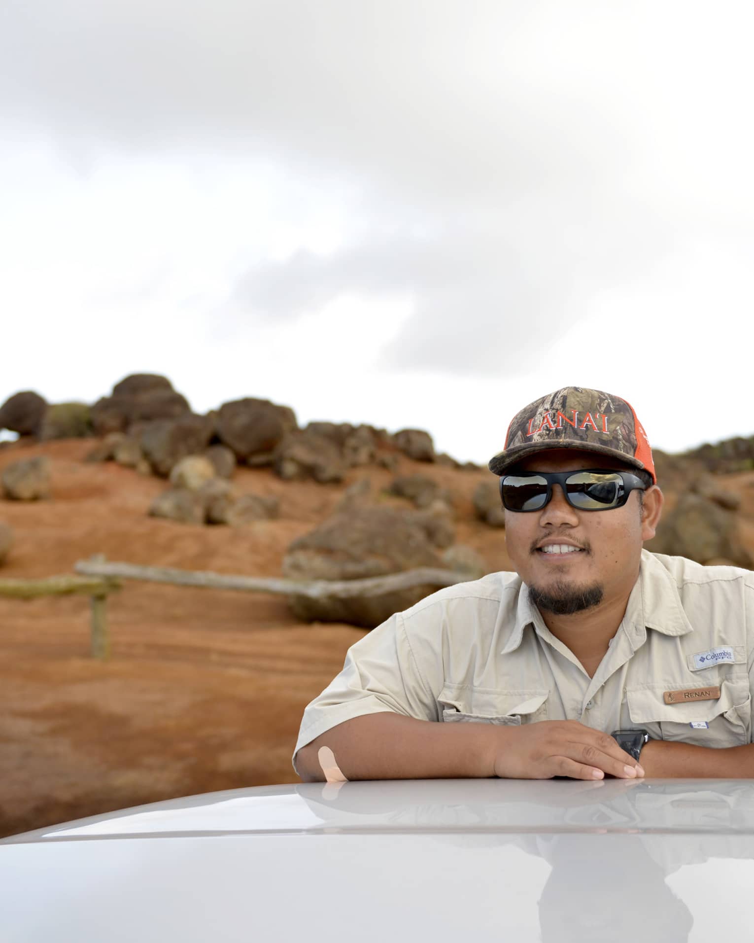 Man leans on top of car, Lanai, Hawaii landscape in the background