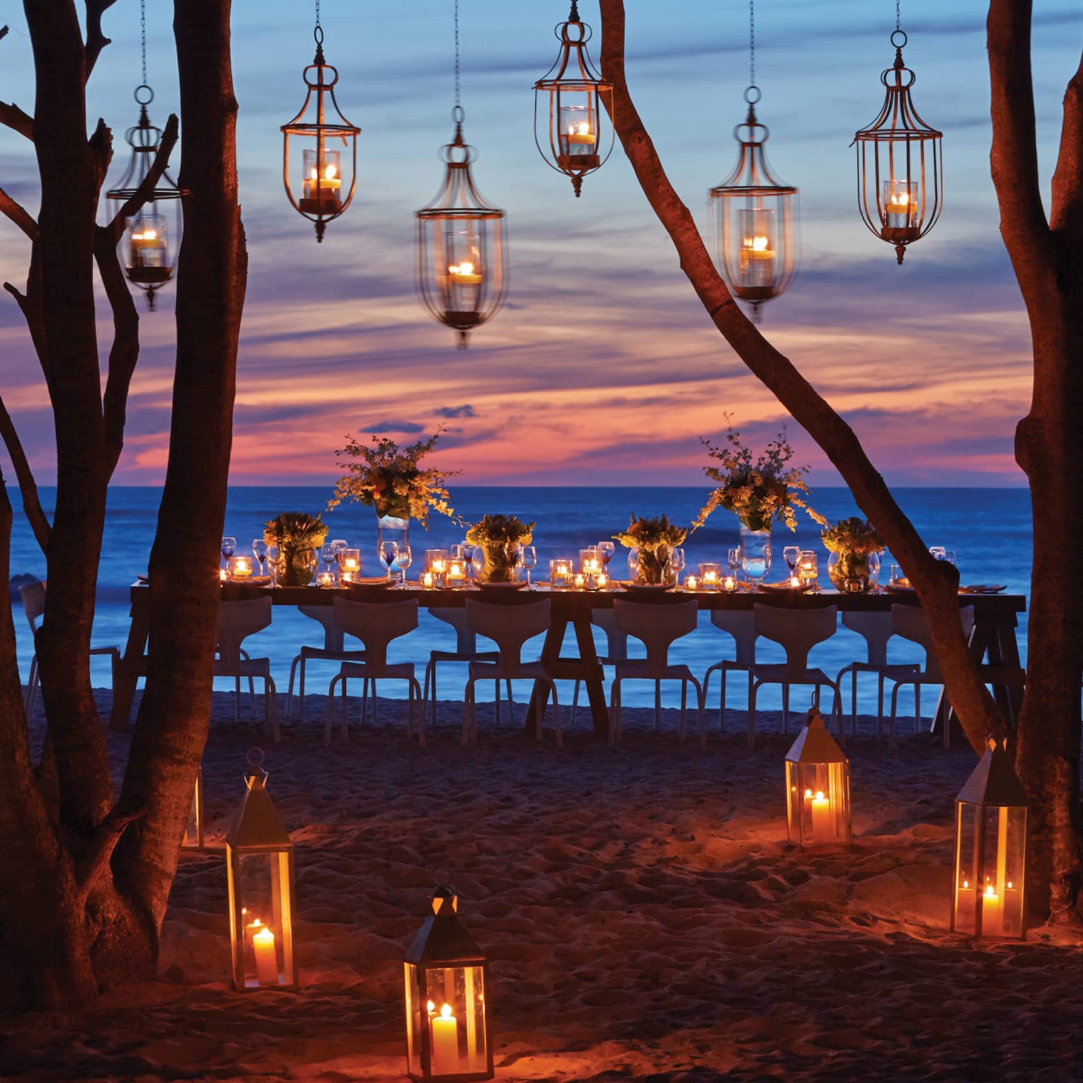 Lanterns hang from trees near dining table on Manzanillas Beach at sunset
