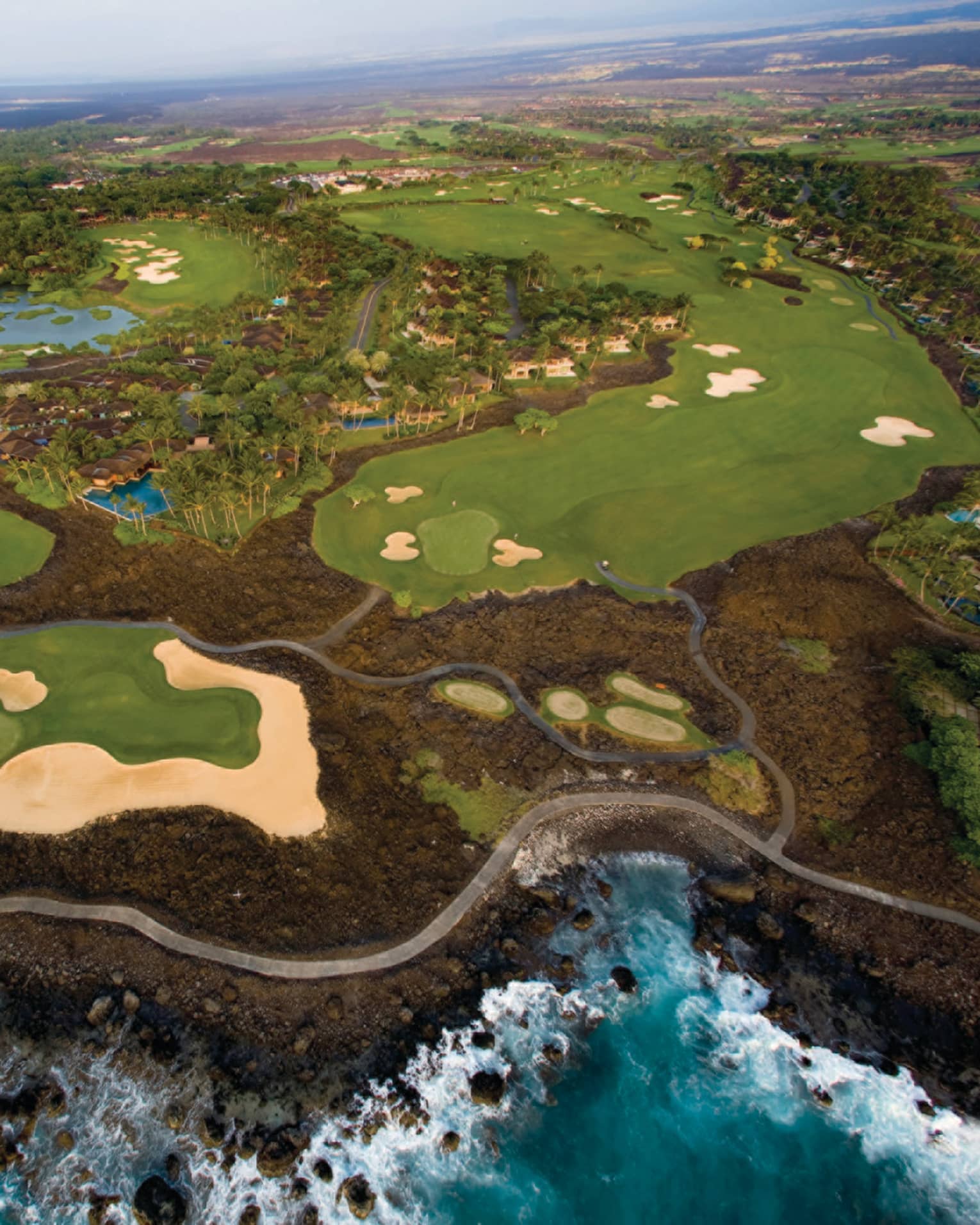 Aerial view of Hualalai Golf Course along rocky shore and ocean
