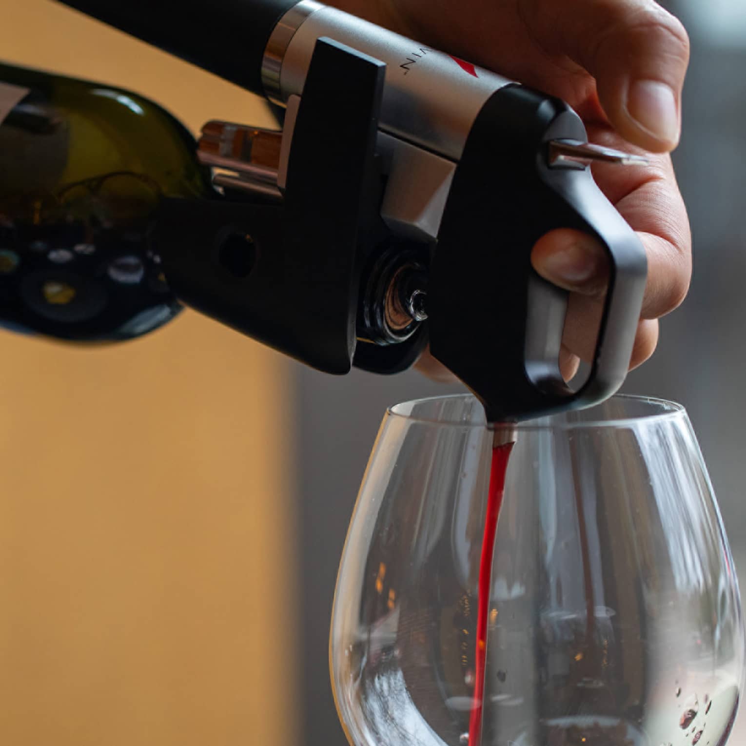 Close-up of a hand using an aerator attached to a wine bottle to pour red wine into a clear, large-bowl stemmed glass.