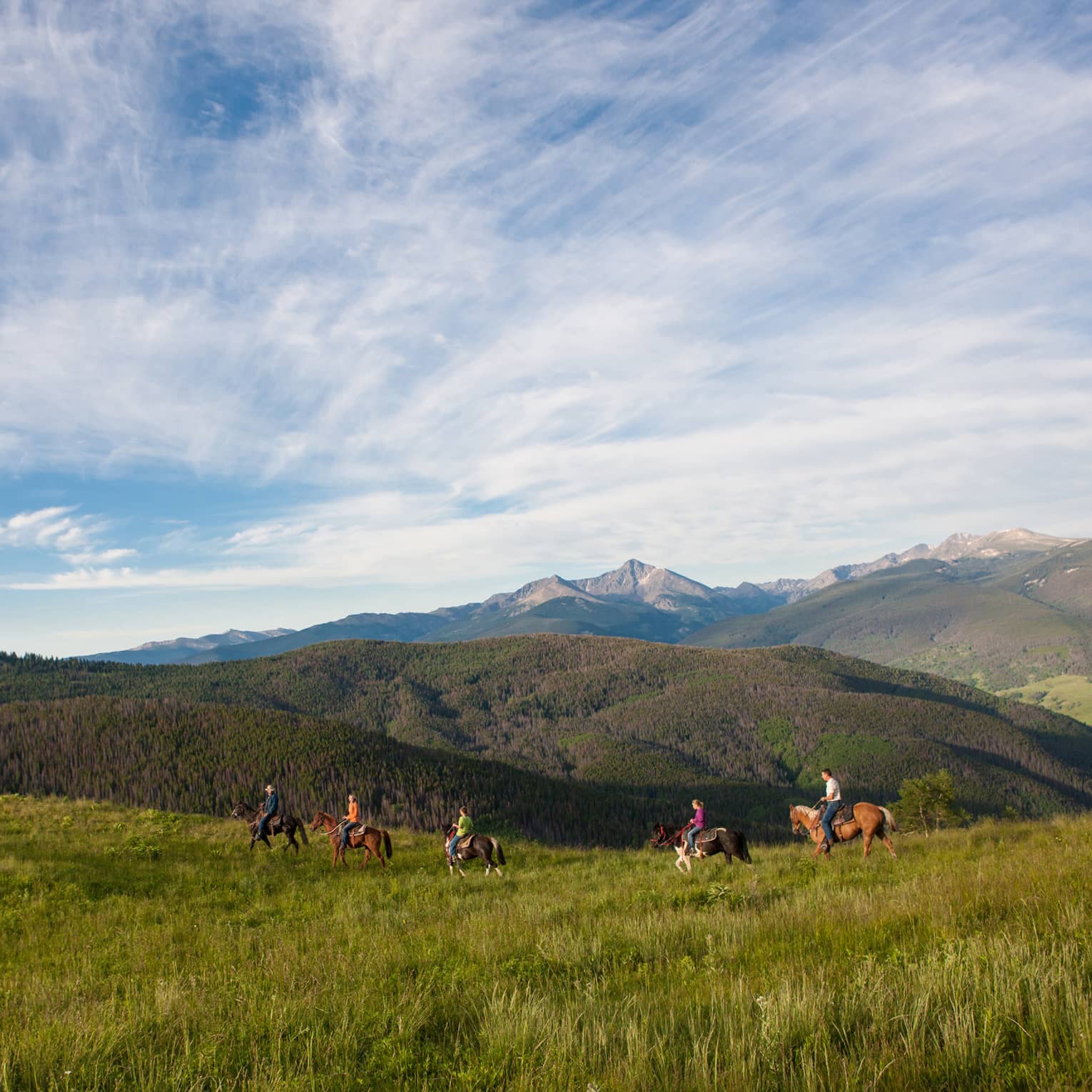 A group of people on horseback riding along grass and hills.