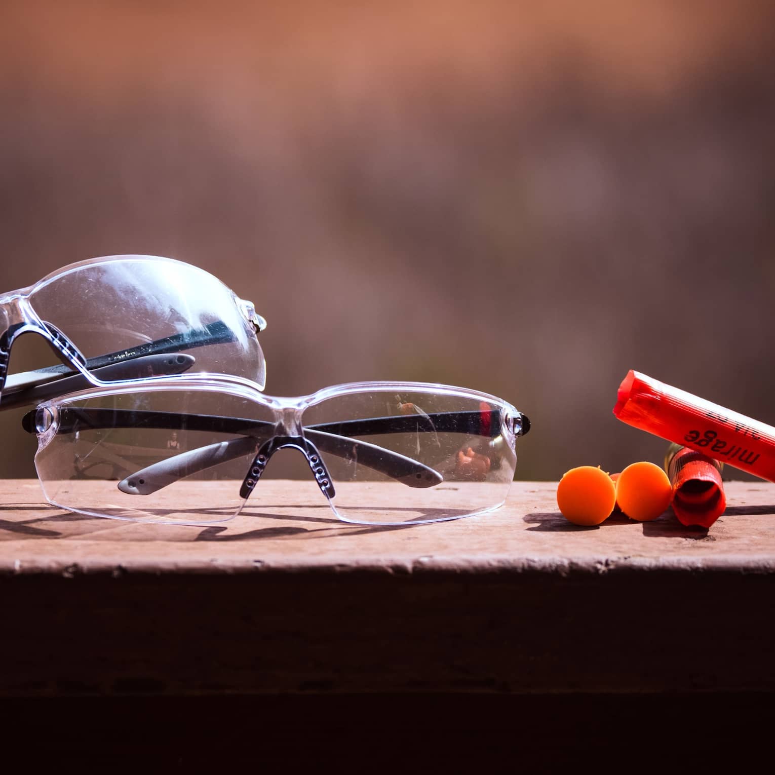 Close-up of two pairs of safety glasses sitting on a dark stone wall aside four spent bullet casings with the word Mirage on.