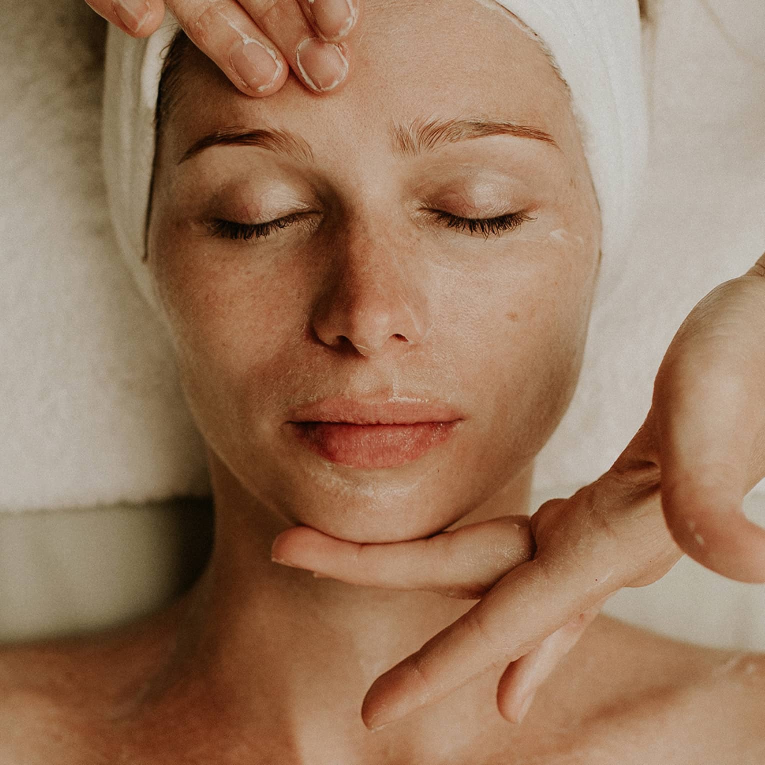Person receiving a relaxing facial massage with eyes closed and head wrapped in a towel