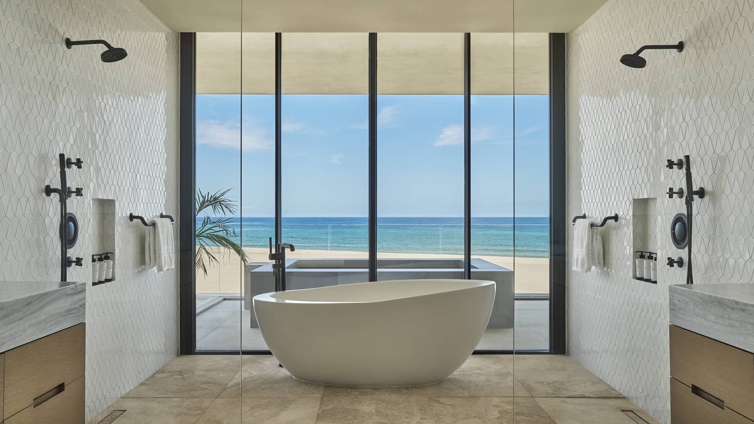 Luxury bathroom with standalone tub, a shower head on each of the two tiled walls, and wall of windows looking out to the sea, at Four Seasons Resort and Residences Los Cabos