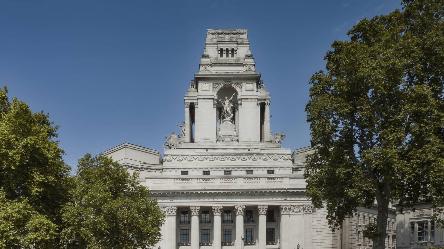 Exterior of Ten Trinity Square Hotel flanked by trees and blue sky in backdrop