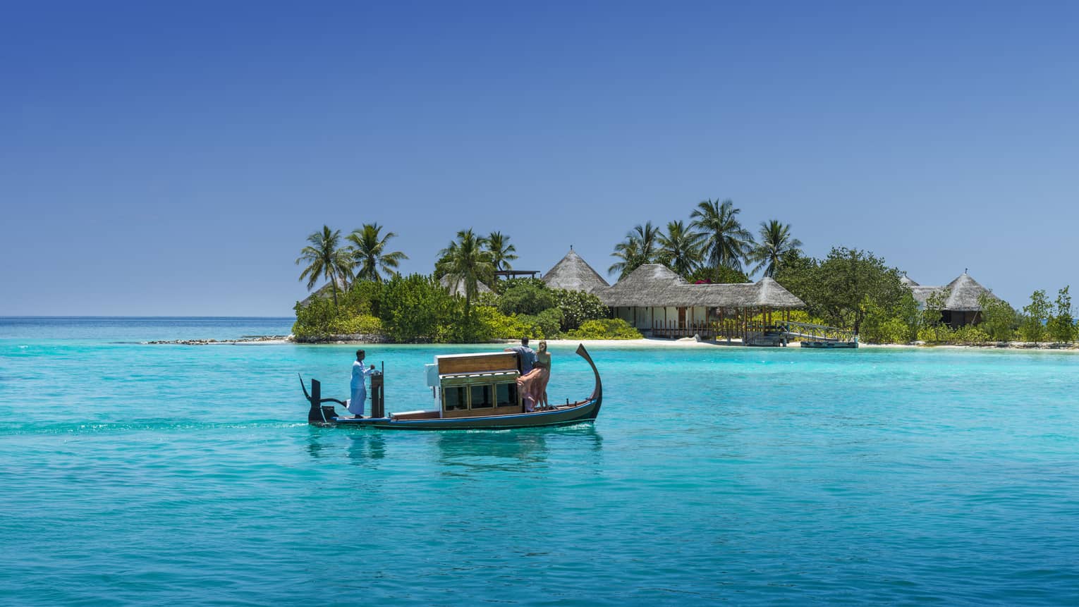 A wooden boat with passengers travels over clear turquoise water toward a tropical island spa with palm trees and thatched-roof villas