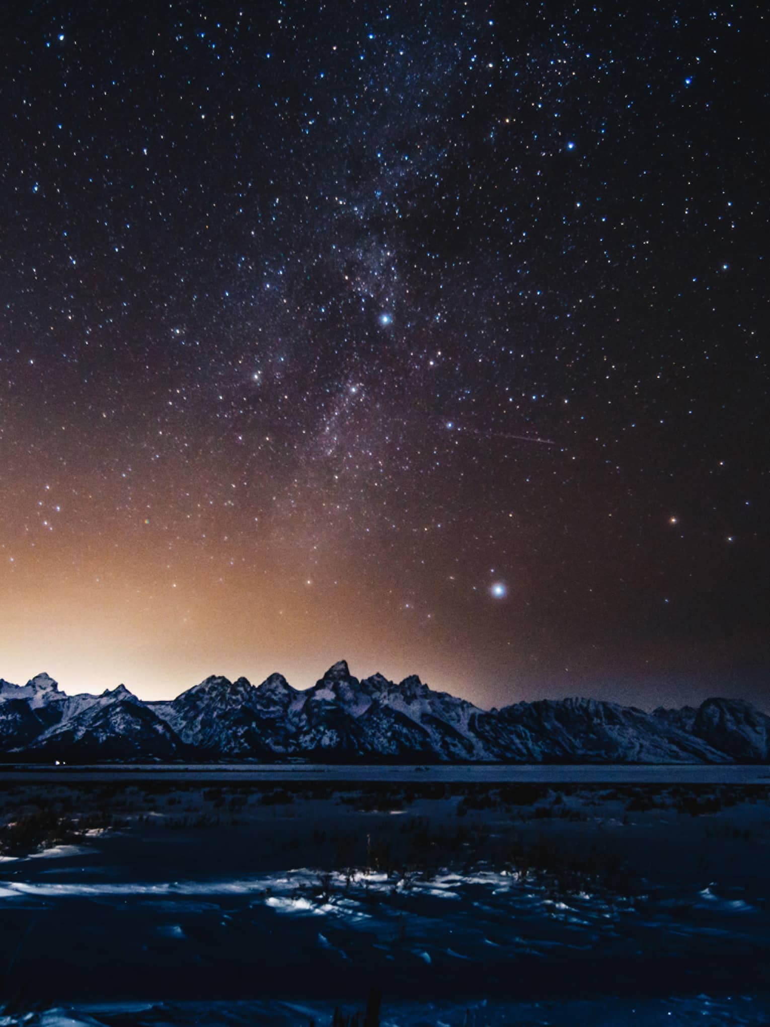 silhouette of mountains and solar flare across the starry night sky in winter