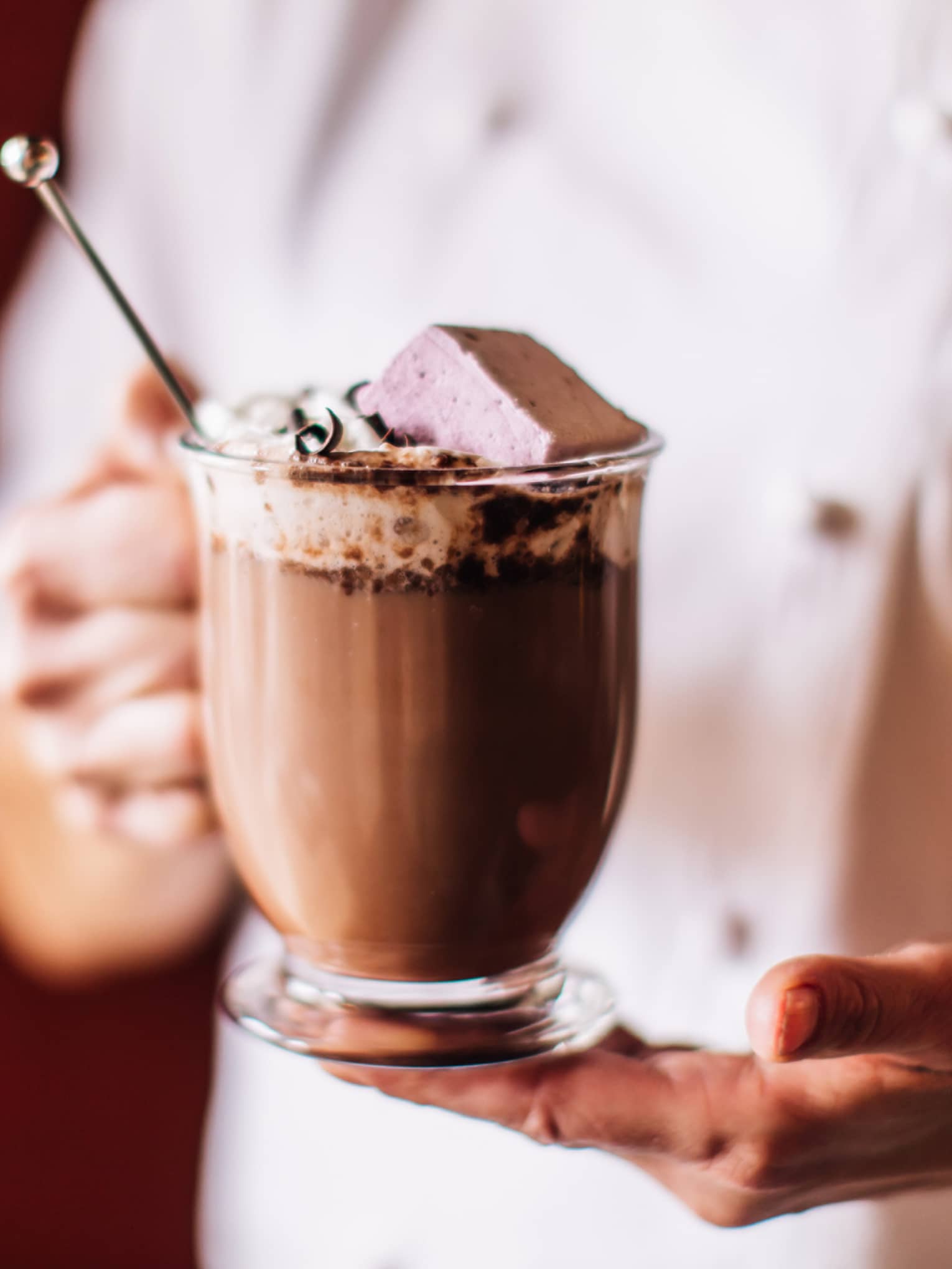 Chef holding a specialty hot chocolate topped with chocolate marshmallow in glass mug