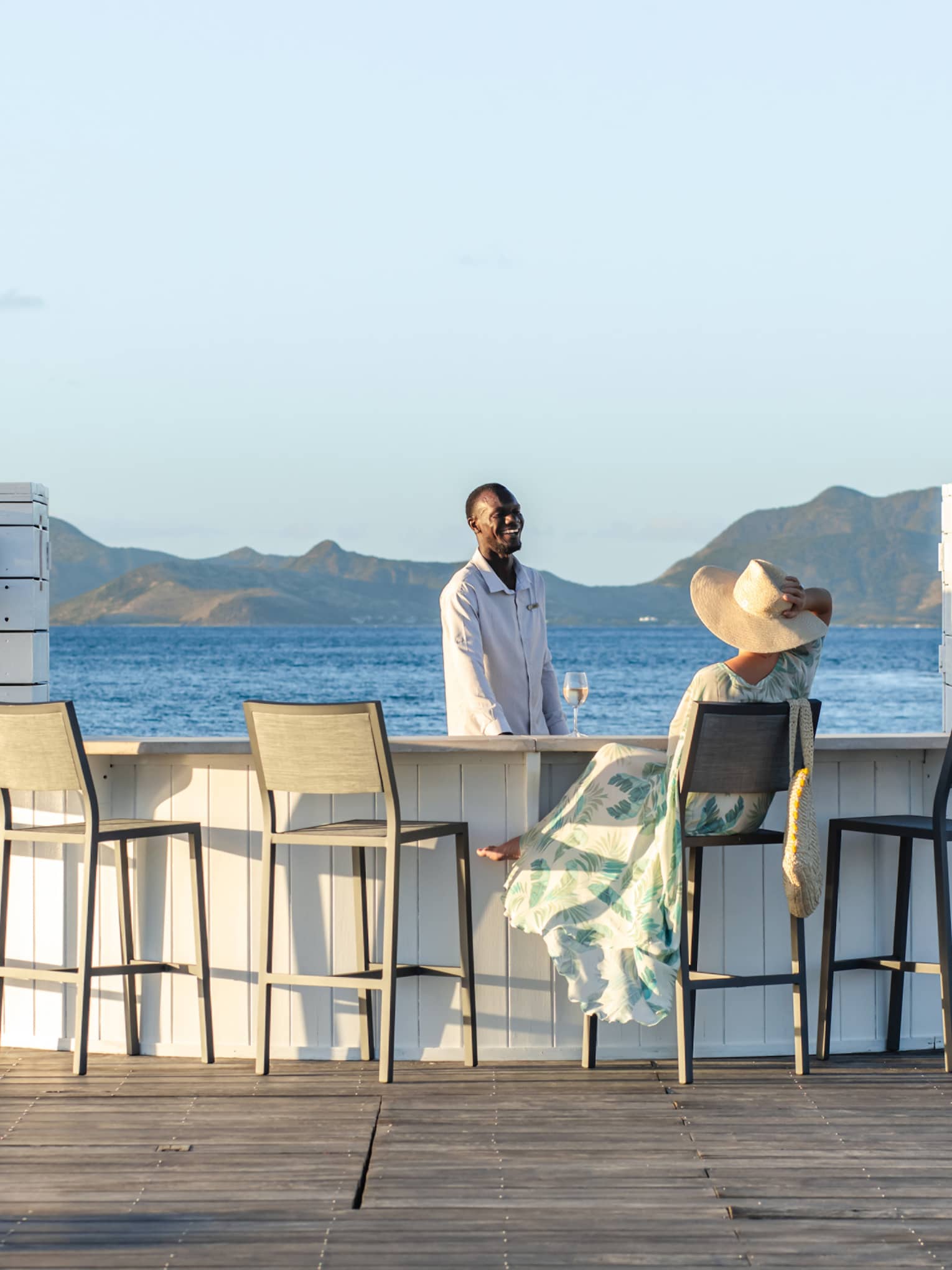 A woman speaks with a bartender at an oceanside bar