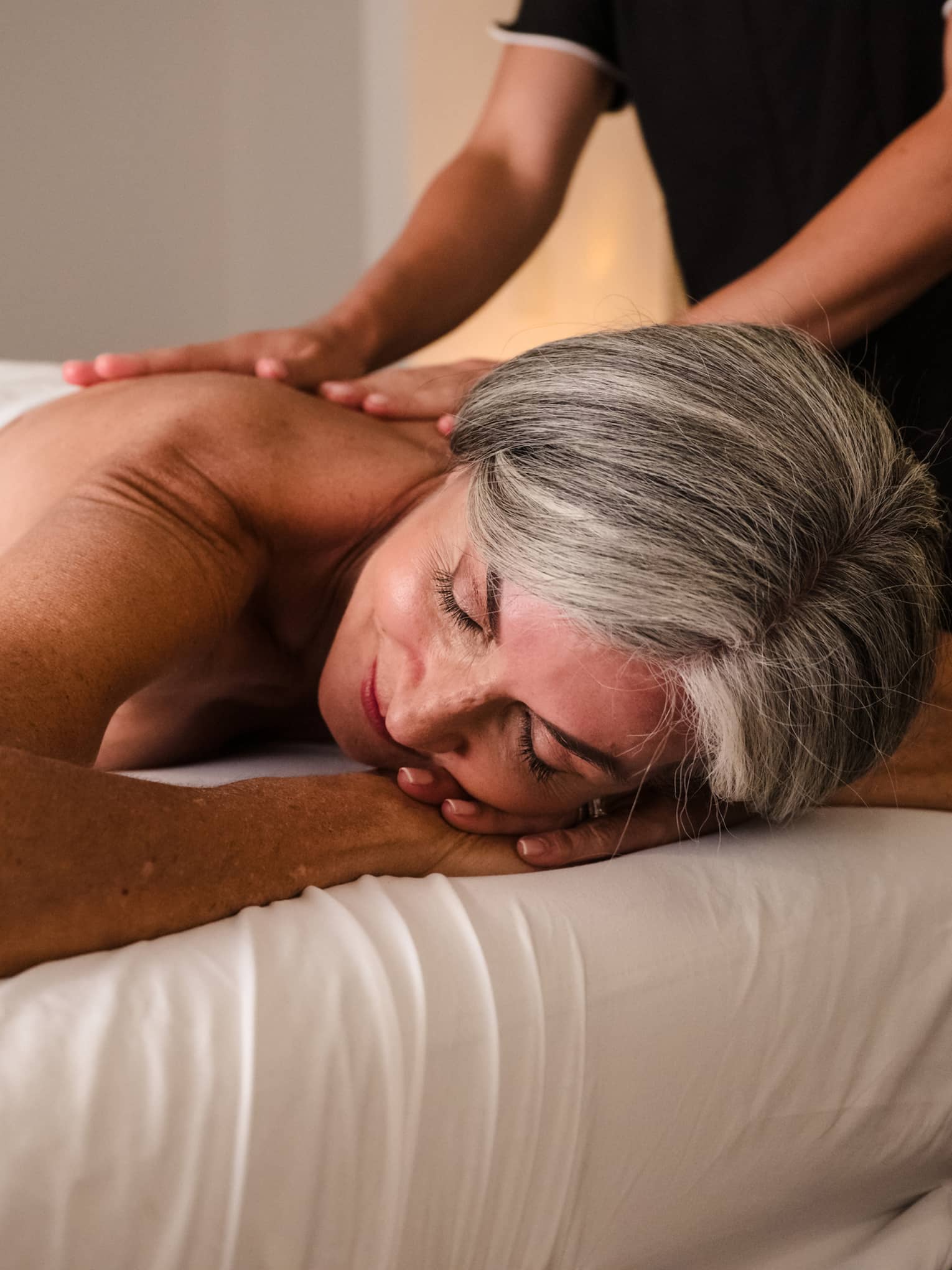 Person lies face down on massage table as therapist in black uniform performs massage