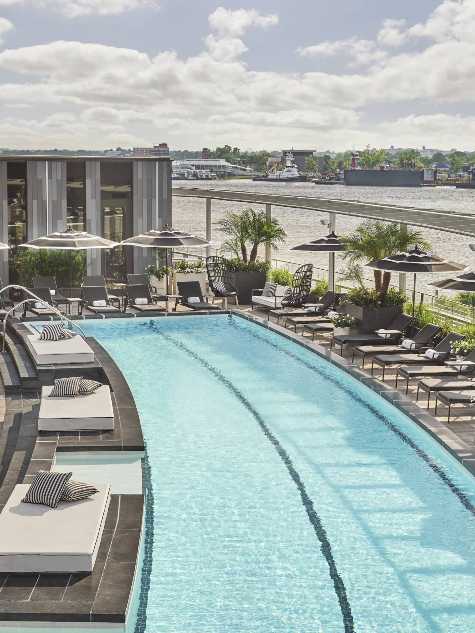 Pool with lounge chairs and umbrellas and a view of the river.