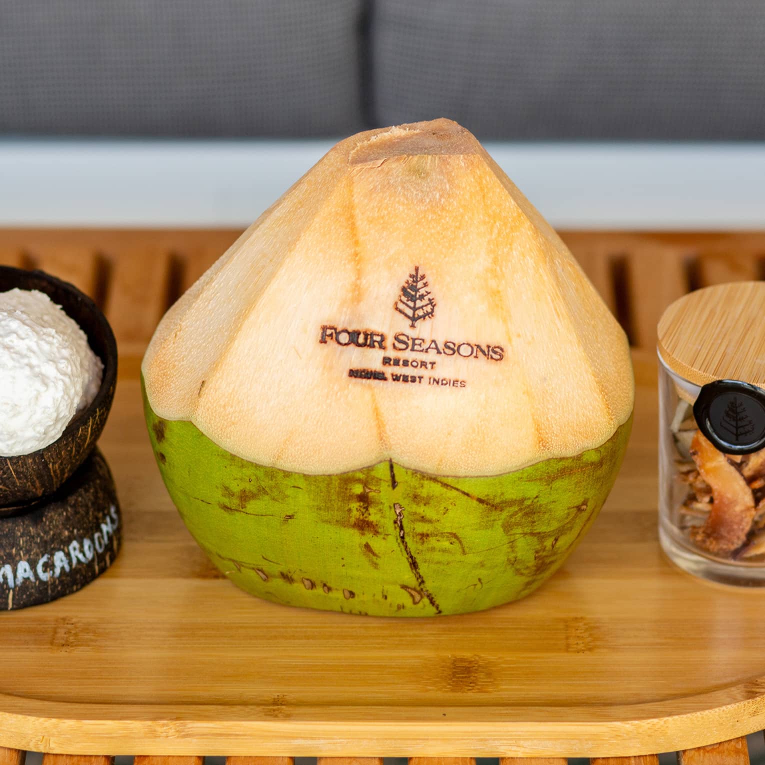 On a wooden platter are coconut macaroons, a fresh coconut carved with the Four Seasons logo and a jar of dried coconut.