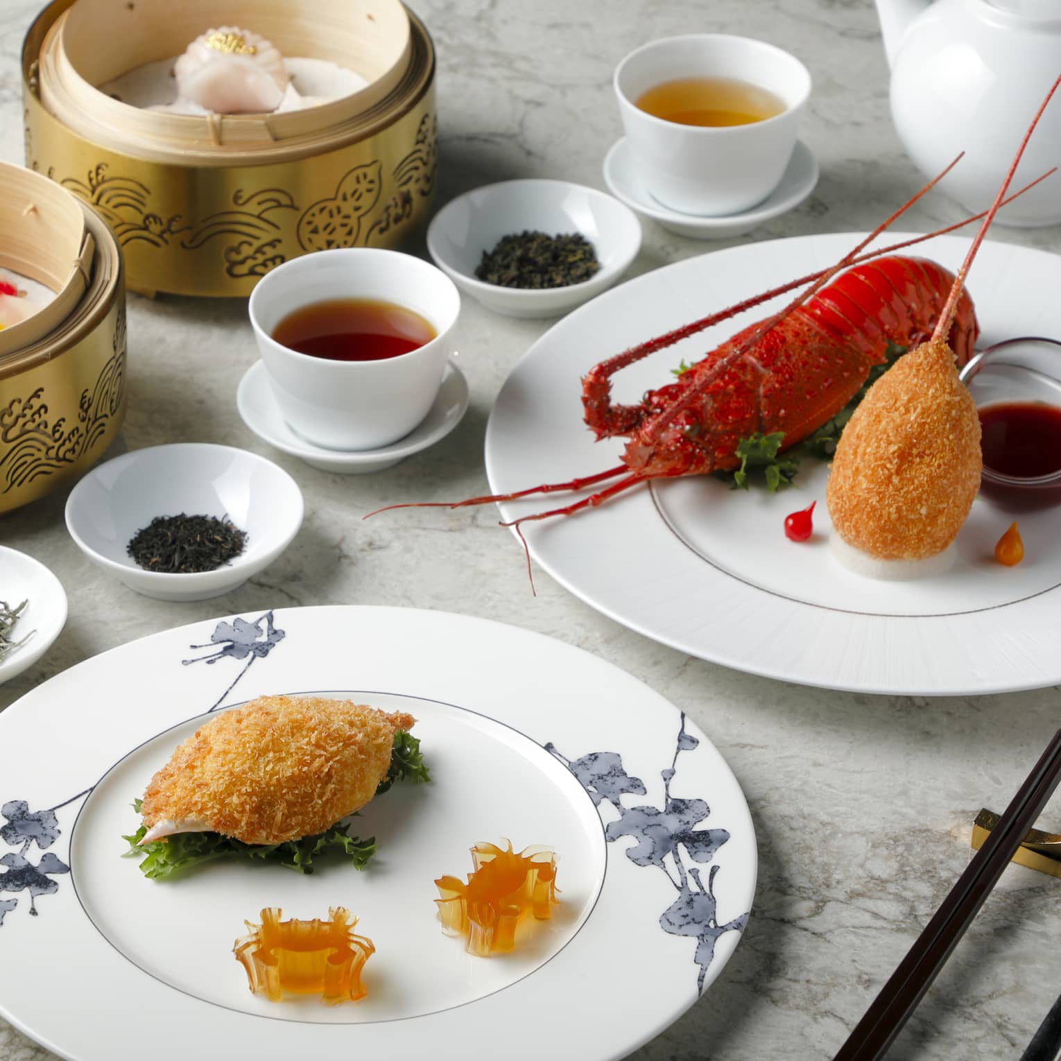 Plain white cups of tea are surrounded by bowls of dried tea leaves, baskets of dumplings and plates of lobster and seafood.