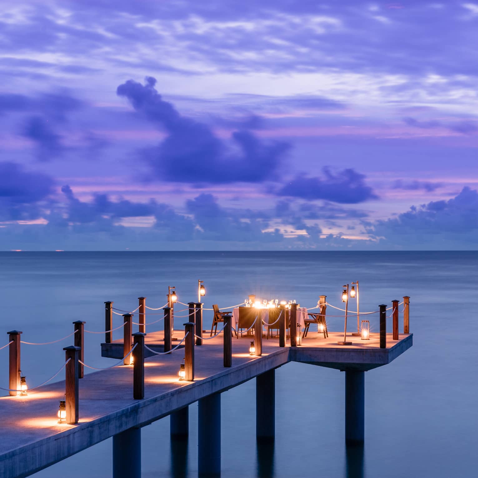 Candlelit jetty off Desroches Island with purple sunset hues