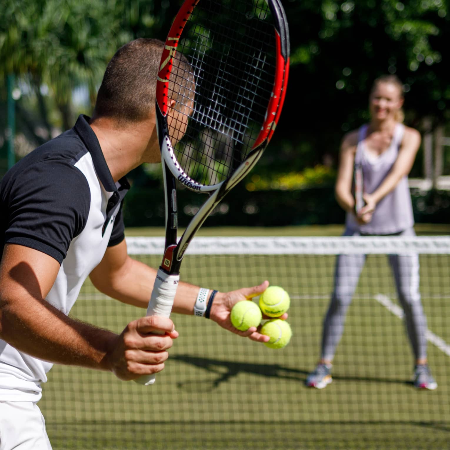 Couple playing tennis on court, man prepares to serve tennis balls to woman ready to swing