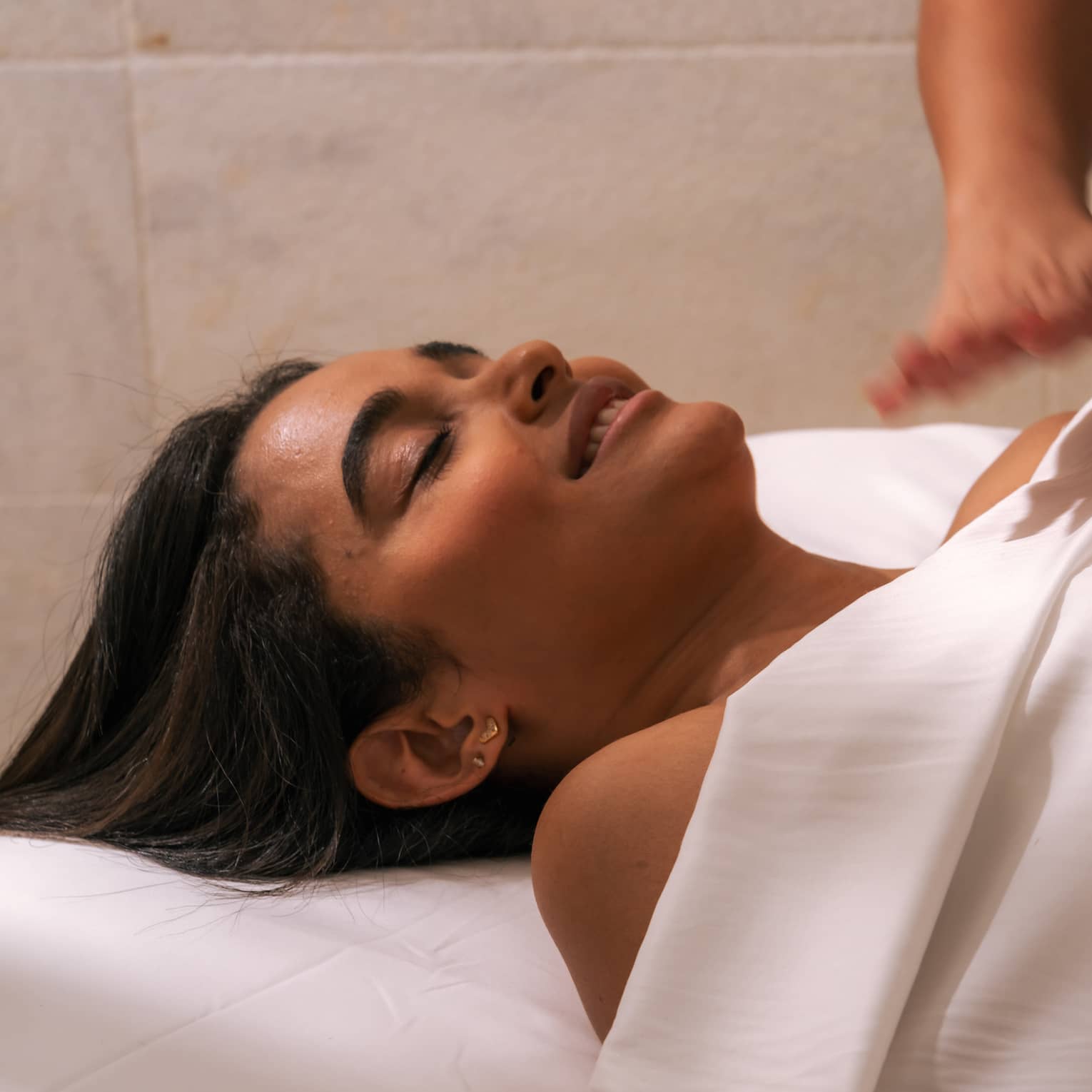 Person lies beneath a white sheet with head and shoulders shown as another person hovers hands over their body