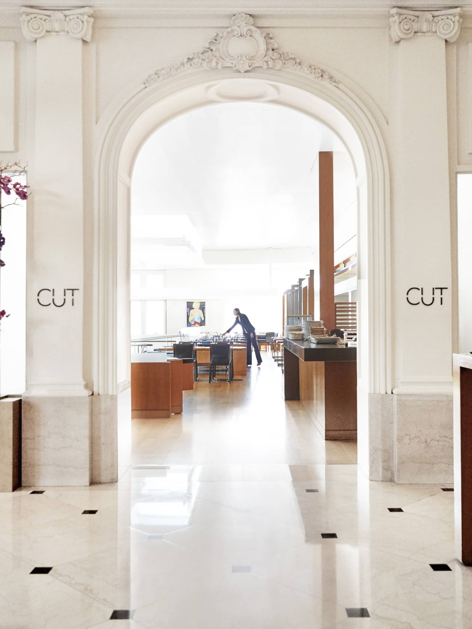 A brightly lit restaurant entrance with cream walls and floor, and a host station made of bright wood.