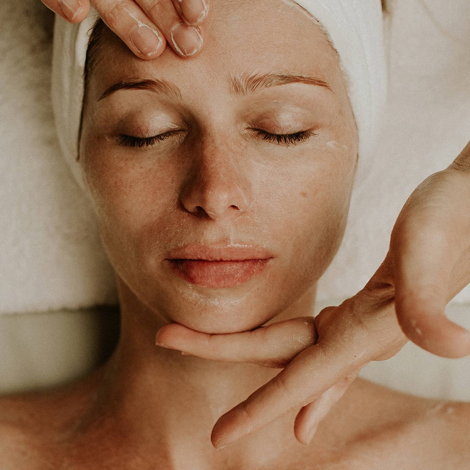 Person receiving a relaxing facial massage with eyes closed and head wrapped in a towel