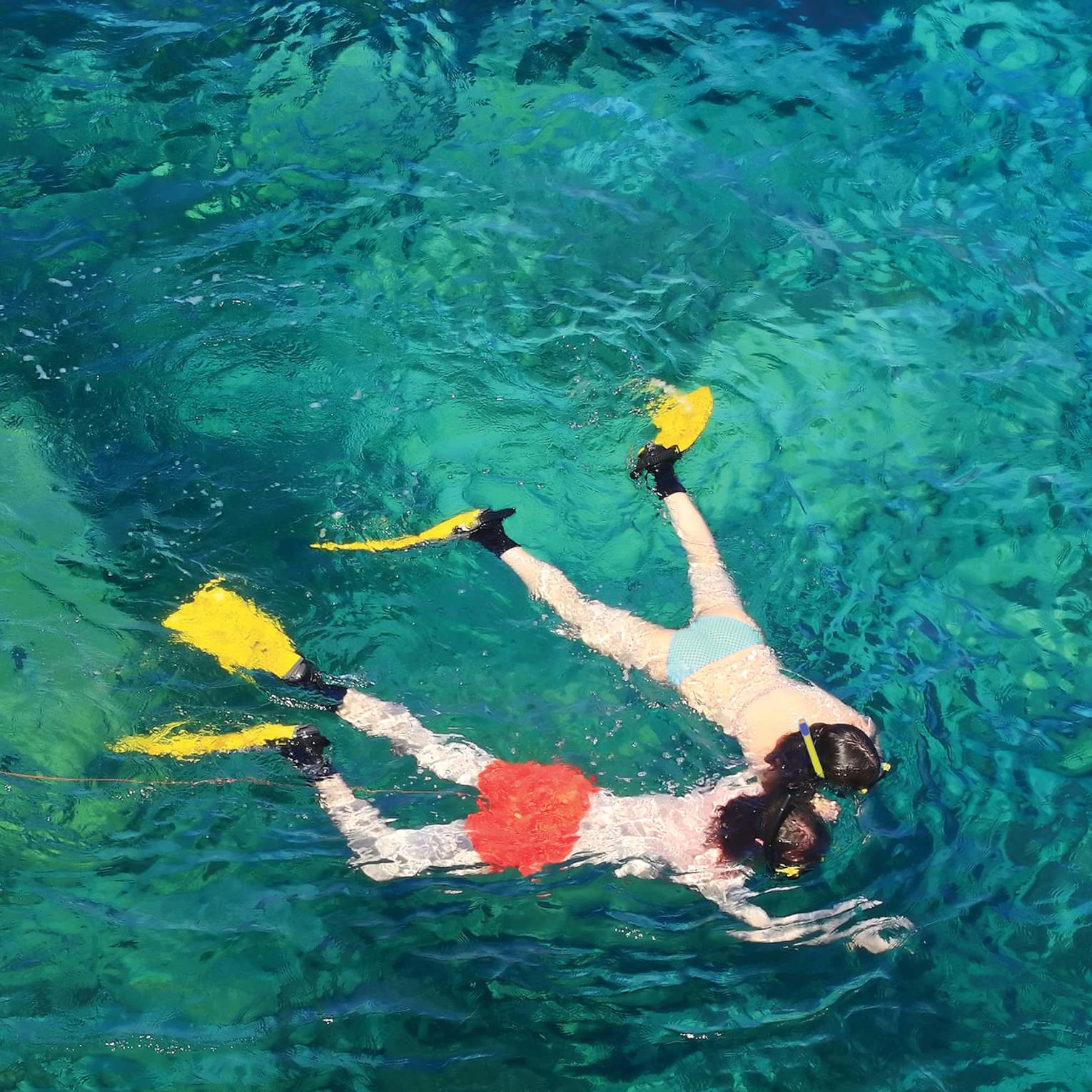 View from above of two guests in flippers snorkelling hand in hand, surrounded by crystal turquoise waters.