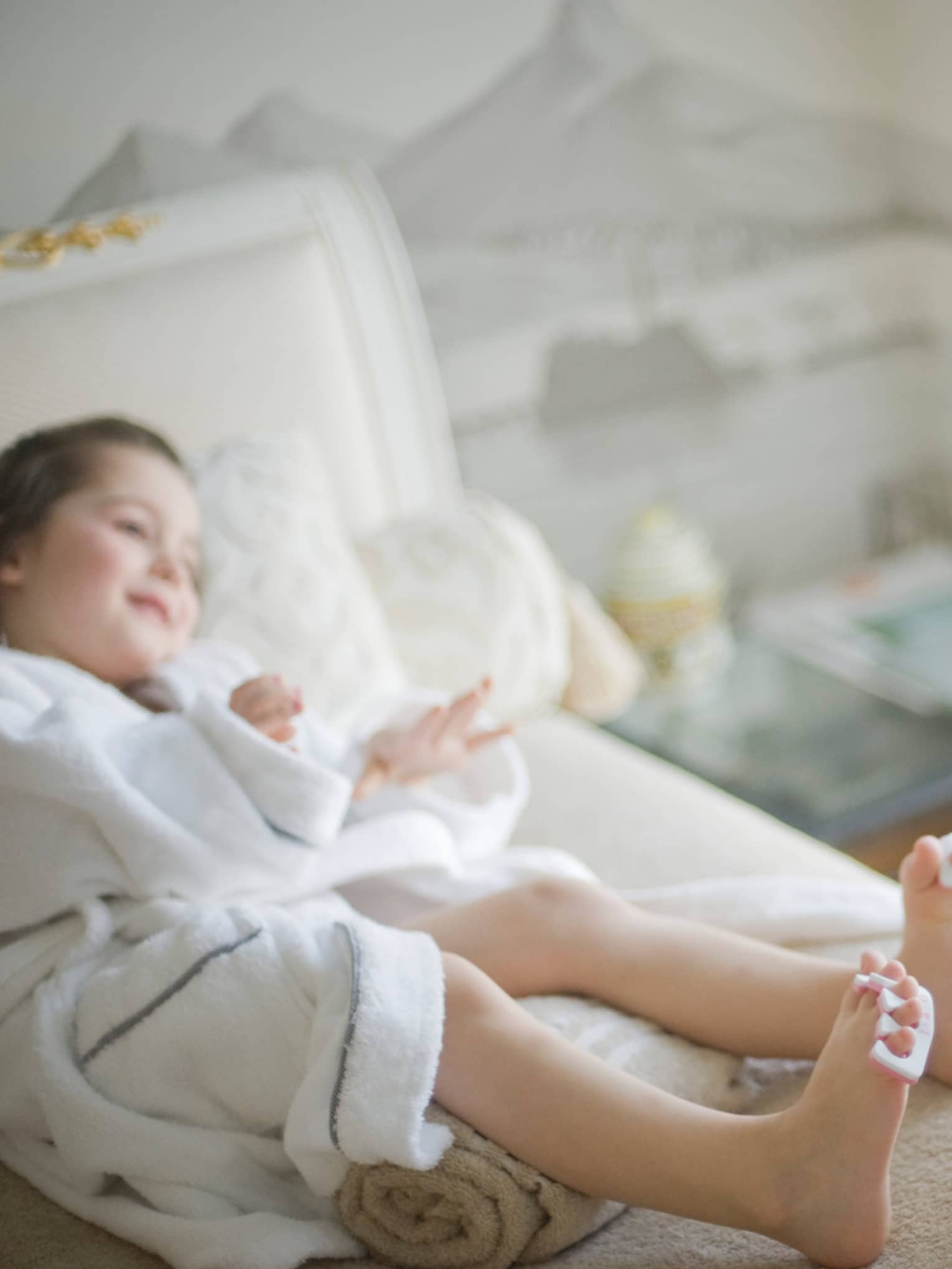 Smiling spa attendant paints toenails of young girl in bathrobe