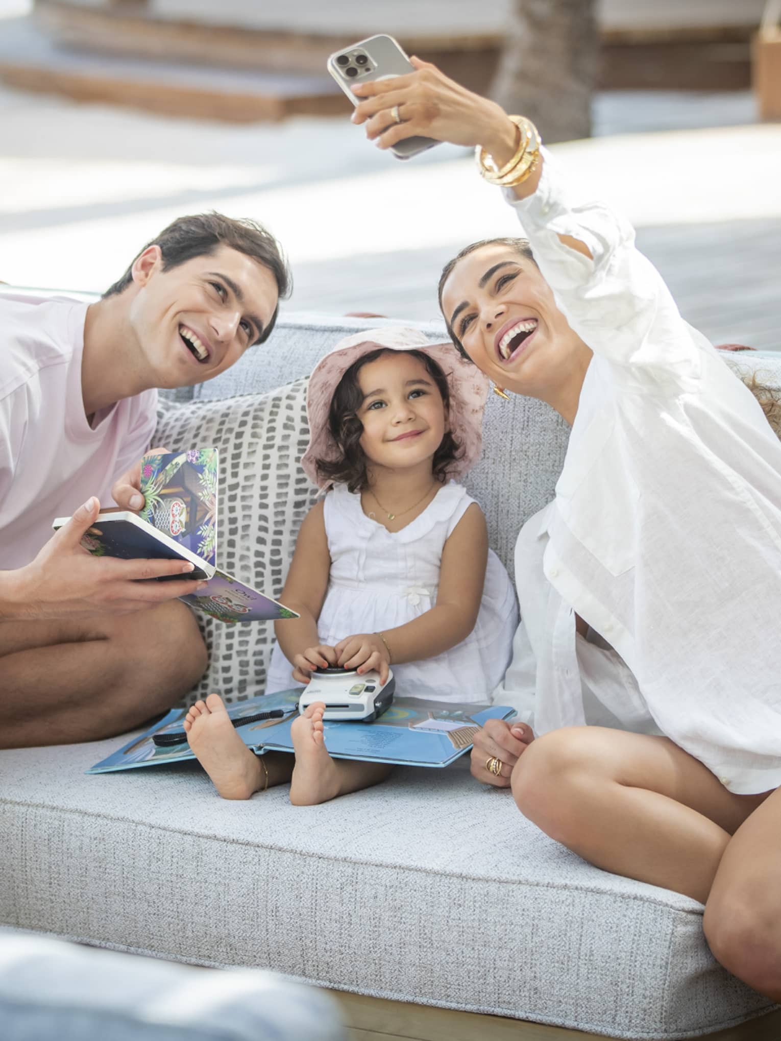 Smiling family of three takes a selfie on outdoor sofa