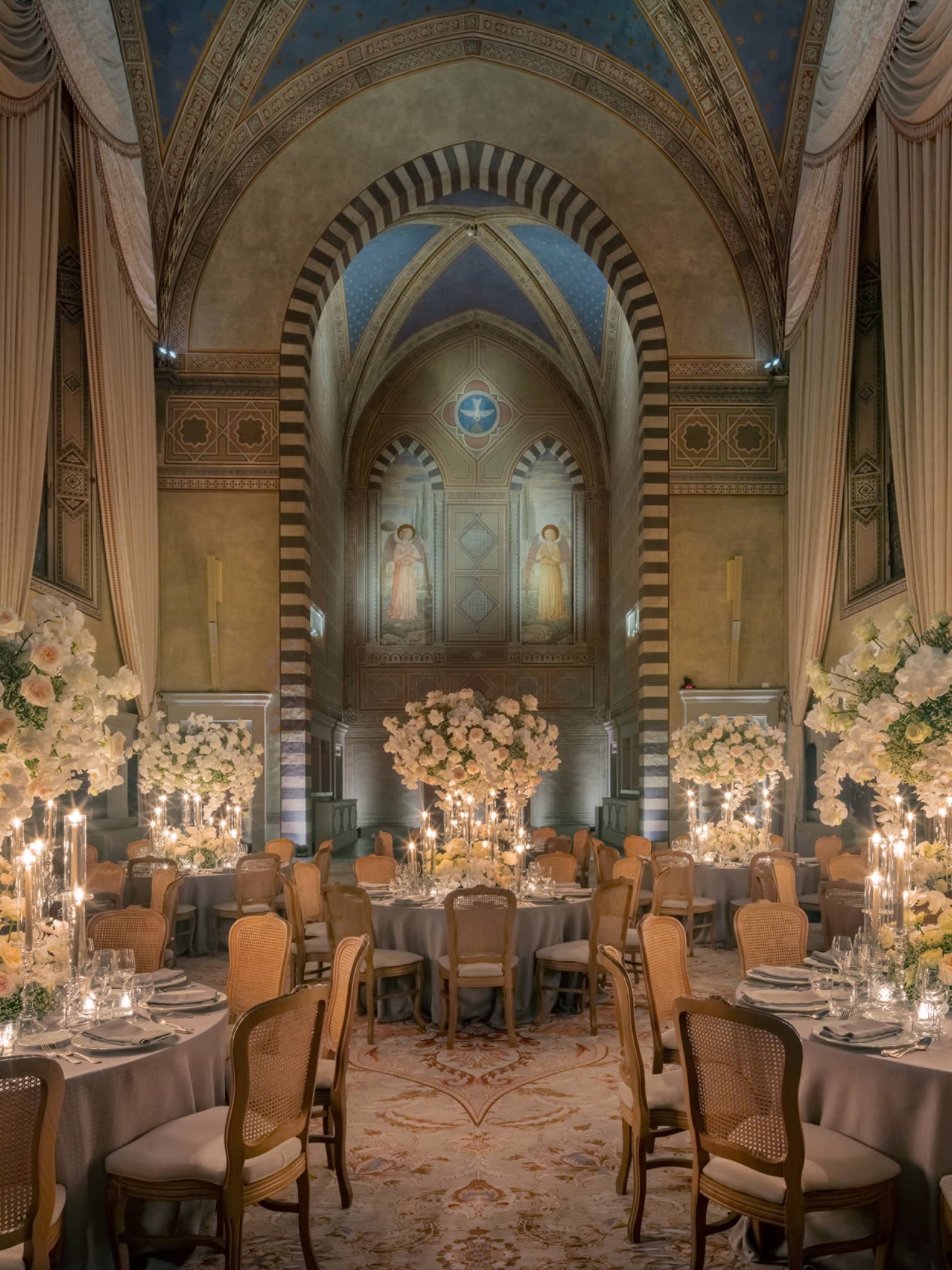 Grand dining room with tall arched ceilings and round elegantly set tables with tall white flower centrepieces