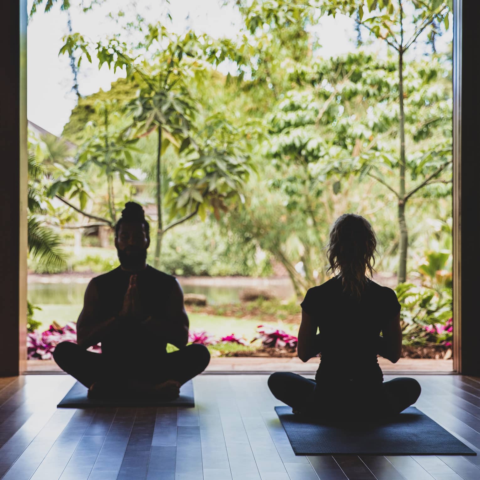 Two people practice yoga in the outdoor covered pavilion surrounded by greenery