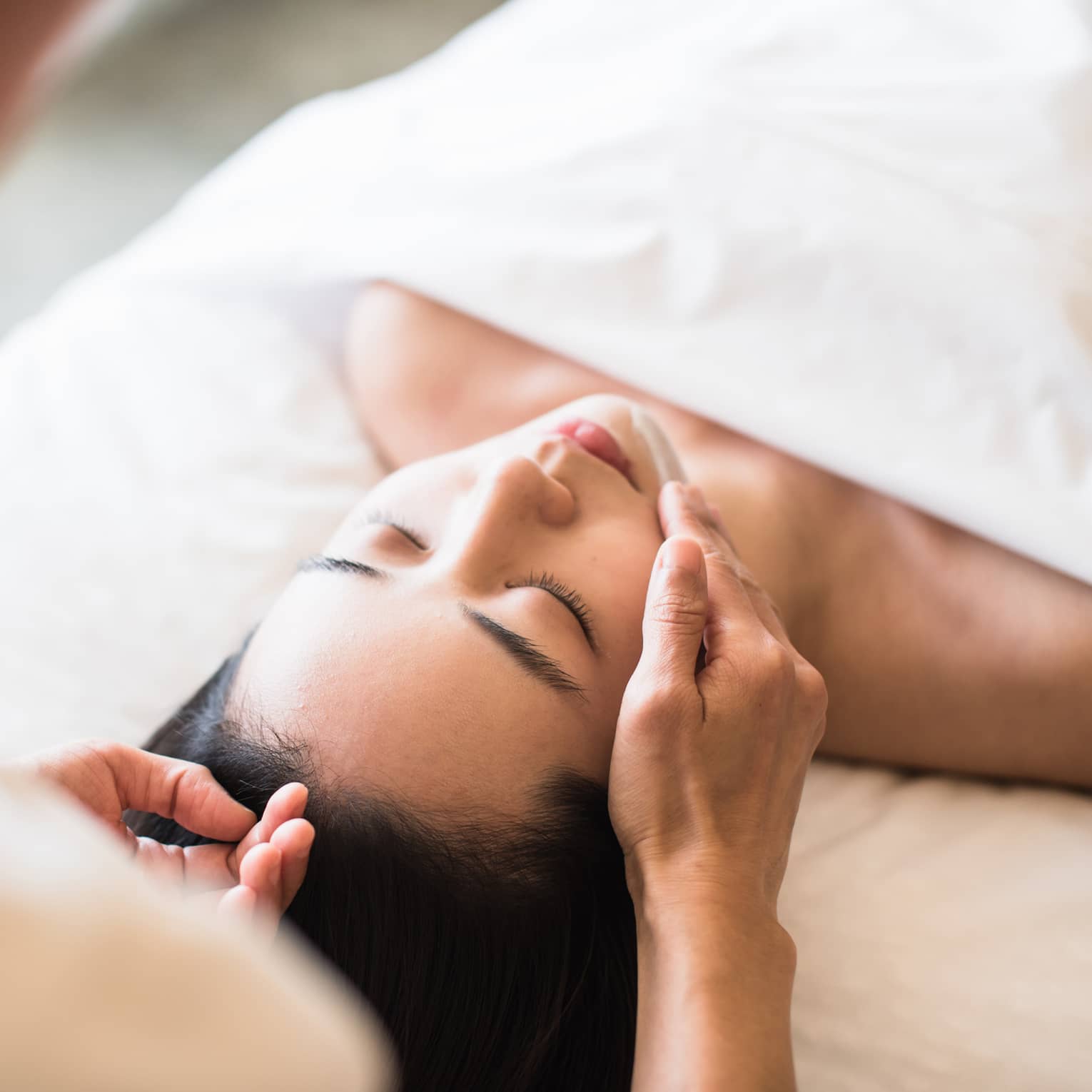 A guest receiving a soothing facial at a spa, lying on a massage table, surrounded by calming décor and soft lighting.