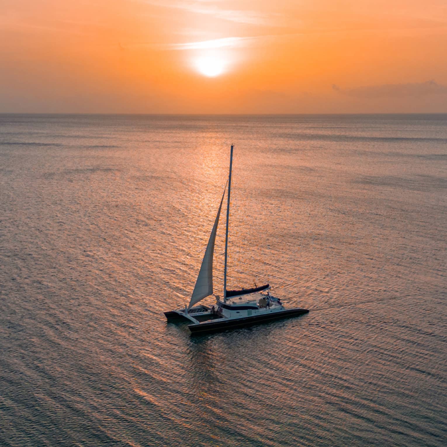 Aerial view of a sailboat floating through calm ocean waters at sunset