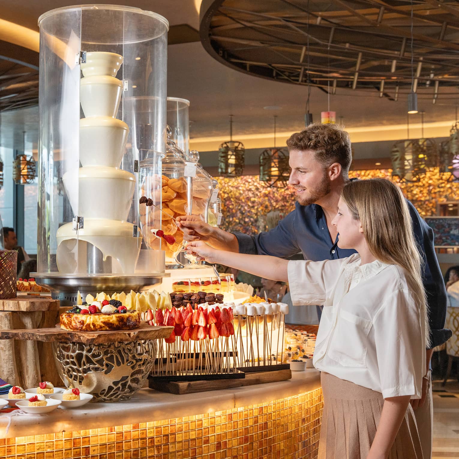 An adult and a child stand in front of a dessert buffet display