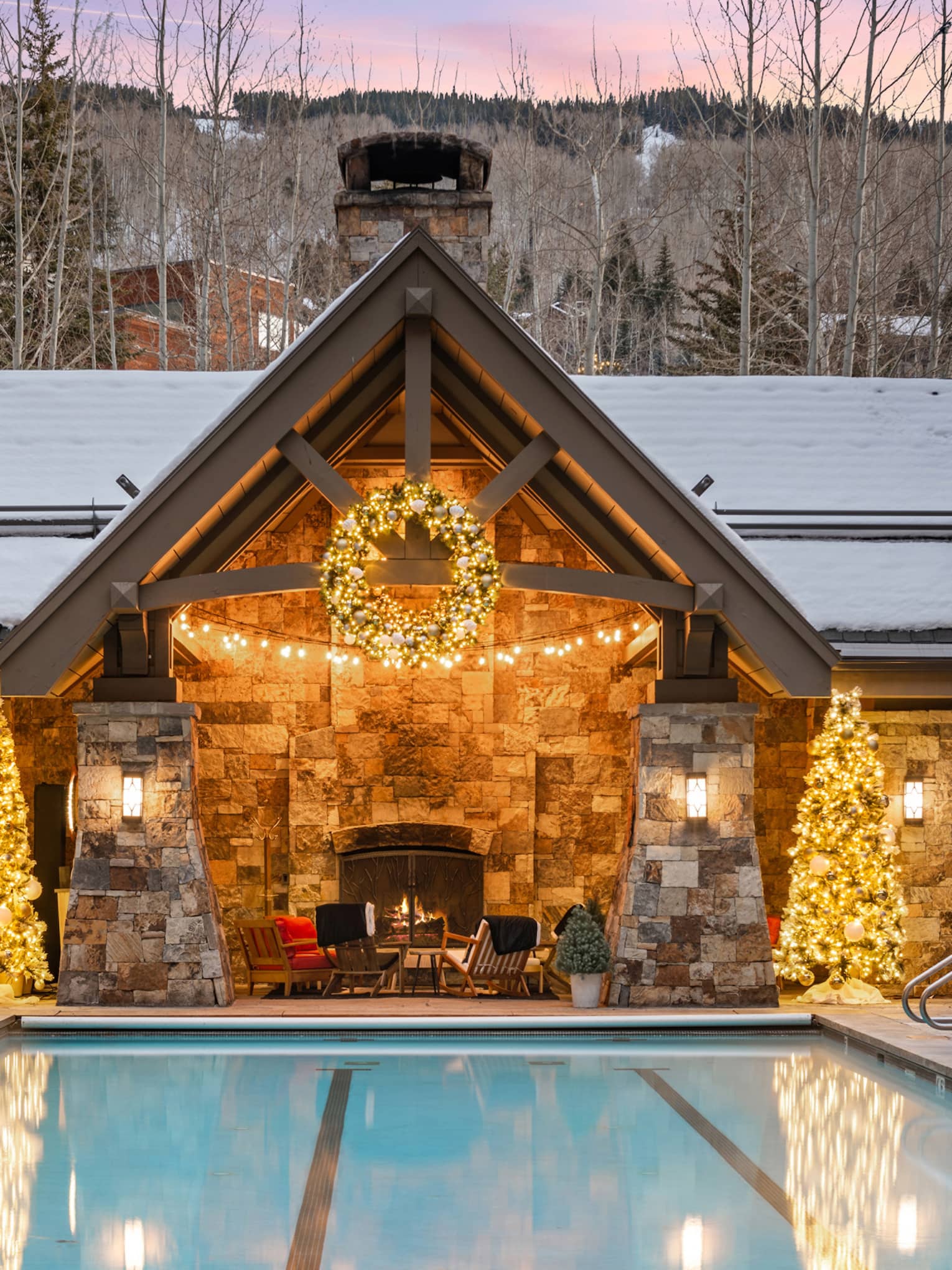 Cabin with two Christmas trees and an outdoor pool with a sunset in the background.