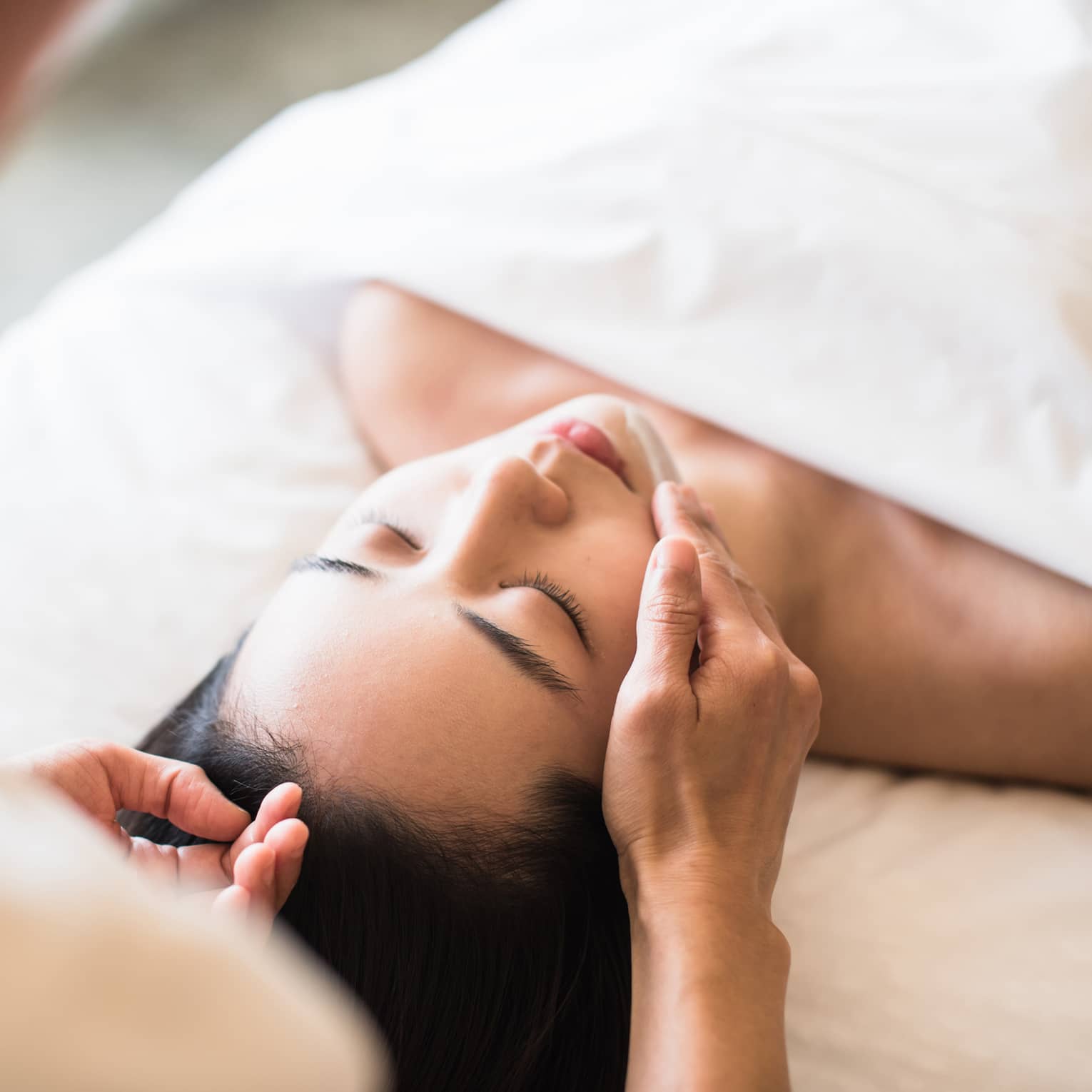 A guest receiving a soothing facial at a spa, lying on a massage table, surrounded by calming décor and soft lighting.