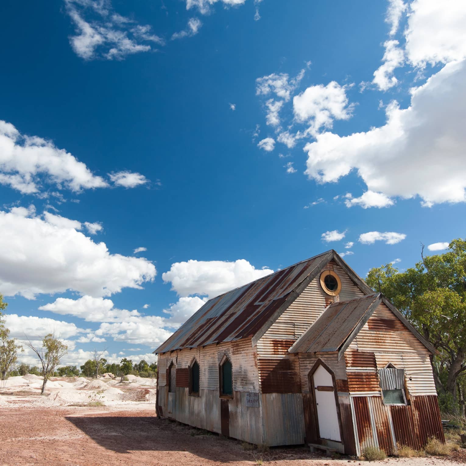 Ramshackle house in Australian outback, sparse trees and blue skies with fluffy clouds