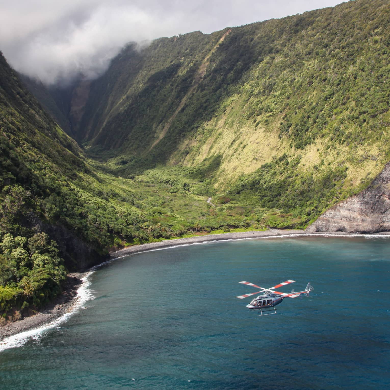 Helicopter flies over ocean by sweeping green volcanic mountains