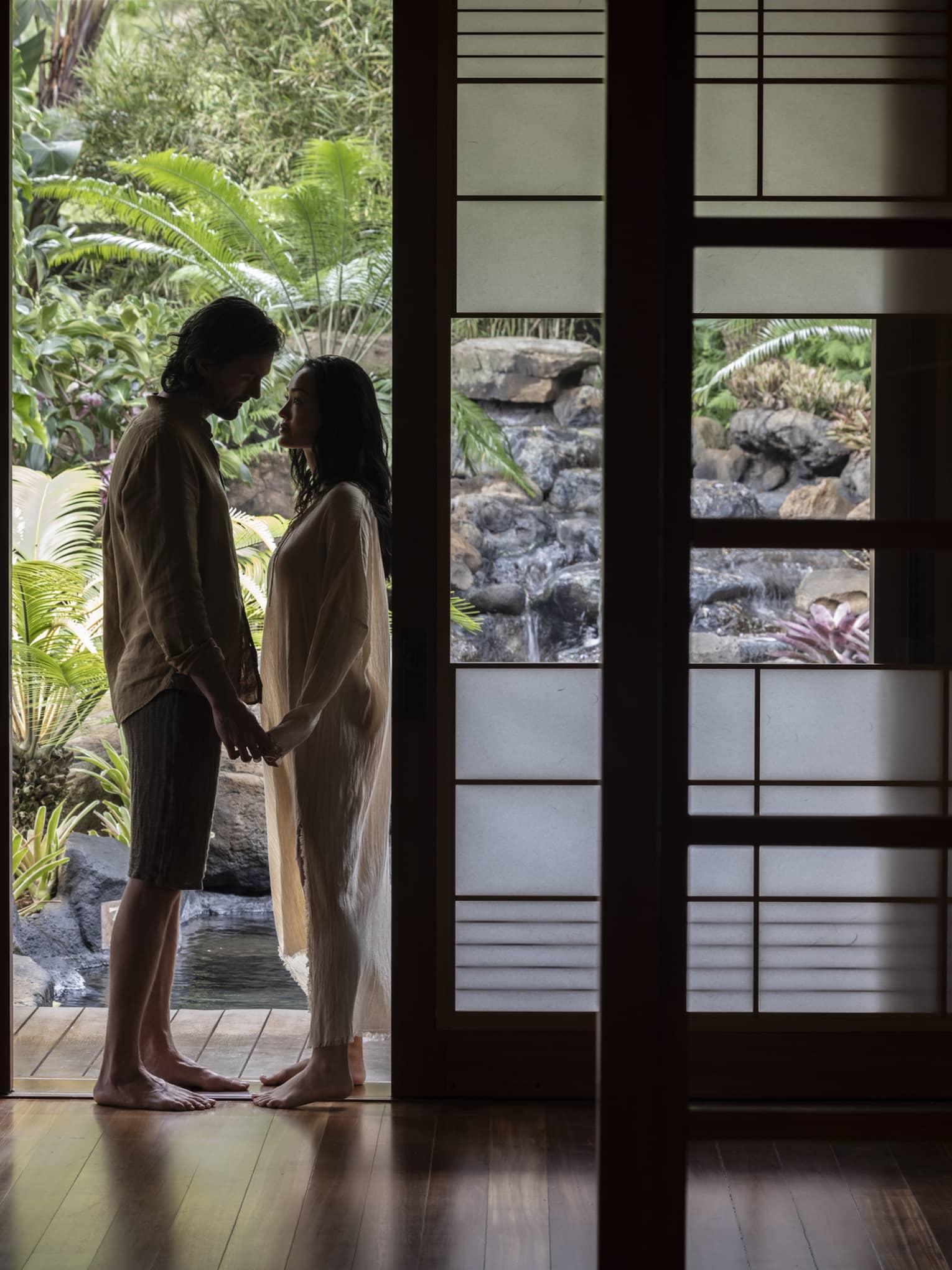 Man and woman stand holding hands in doorway of private spa hale at Sensei Lanai, A Four Seasons Resort