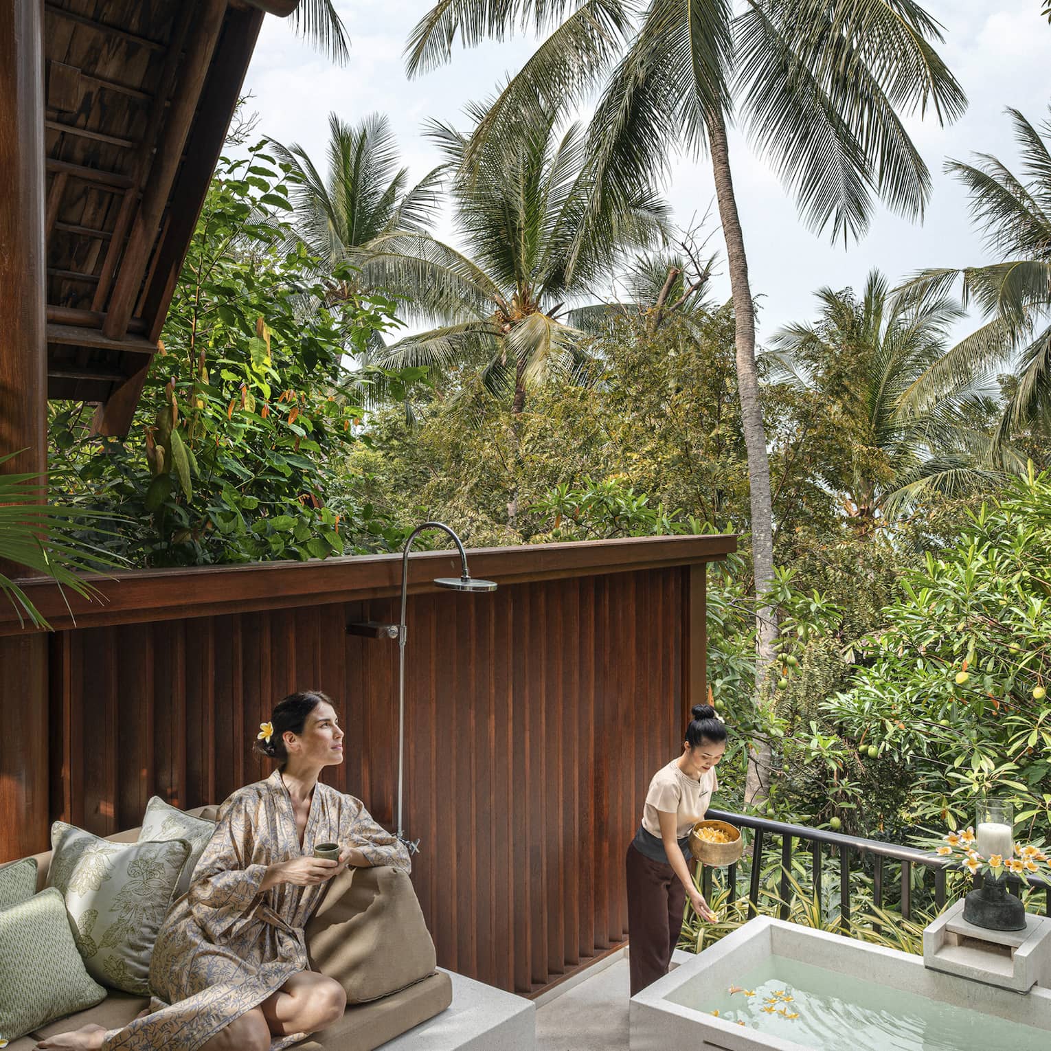 Woman in silk robe lounges on outdoor sofa at the resort spa amidst the lush green garden.