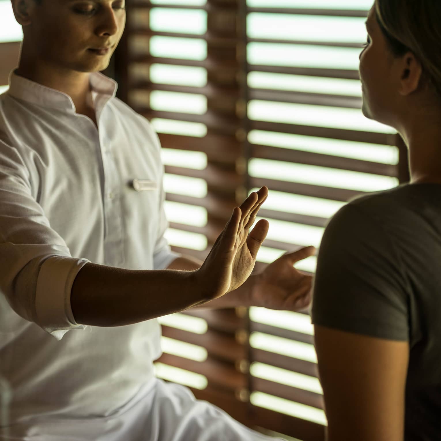 Reiki healer with eyes closed holds hand over woman's body