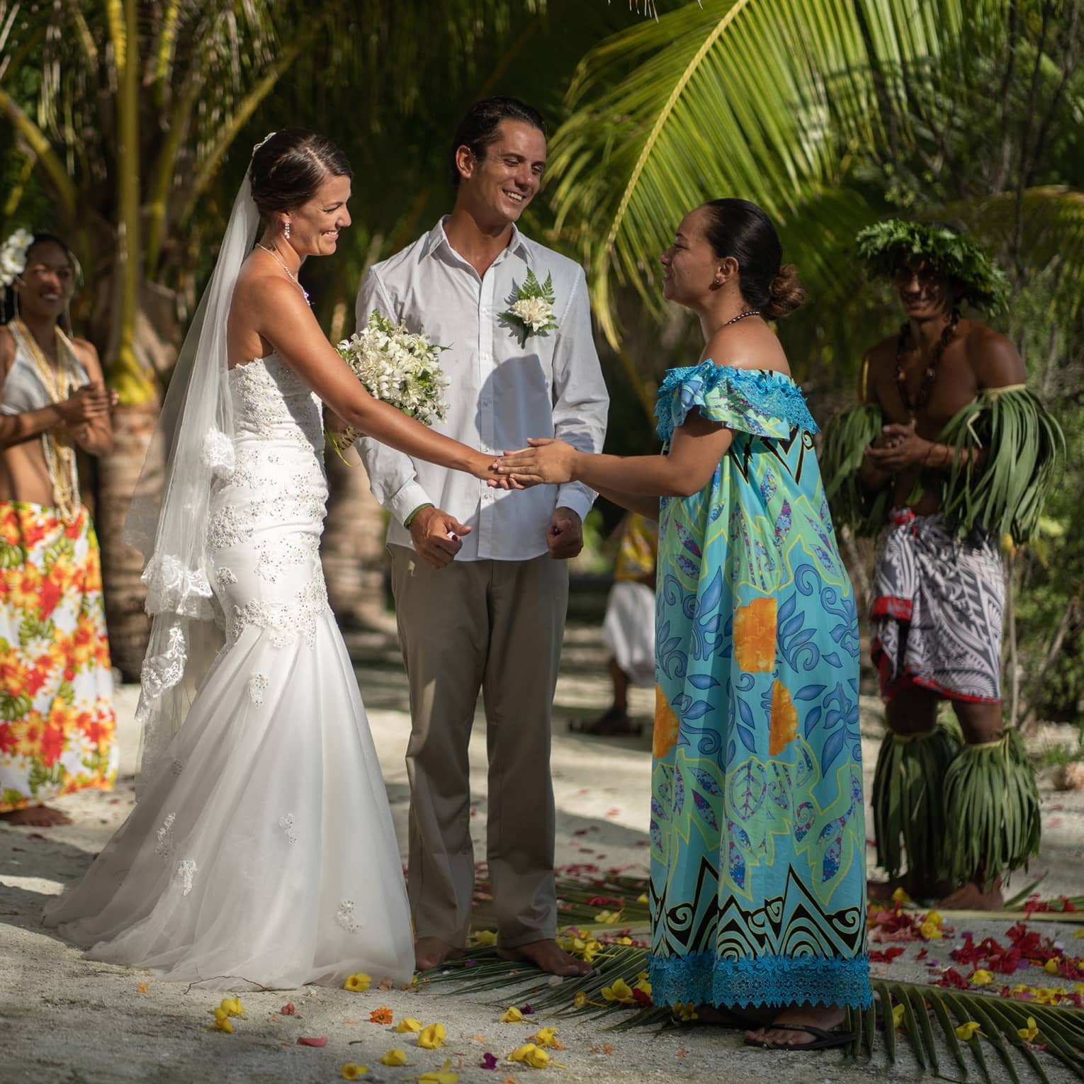 Wedding ceremony on beach, Tahitian woman holds bride's hand