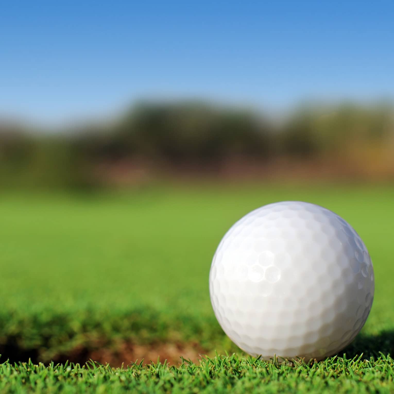 A close up of a white golf ball sitting right next to a golf hole on the course