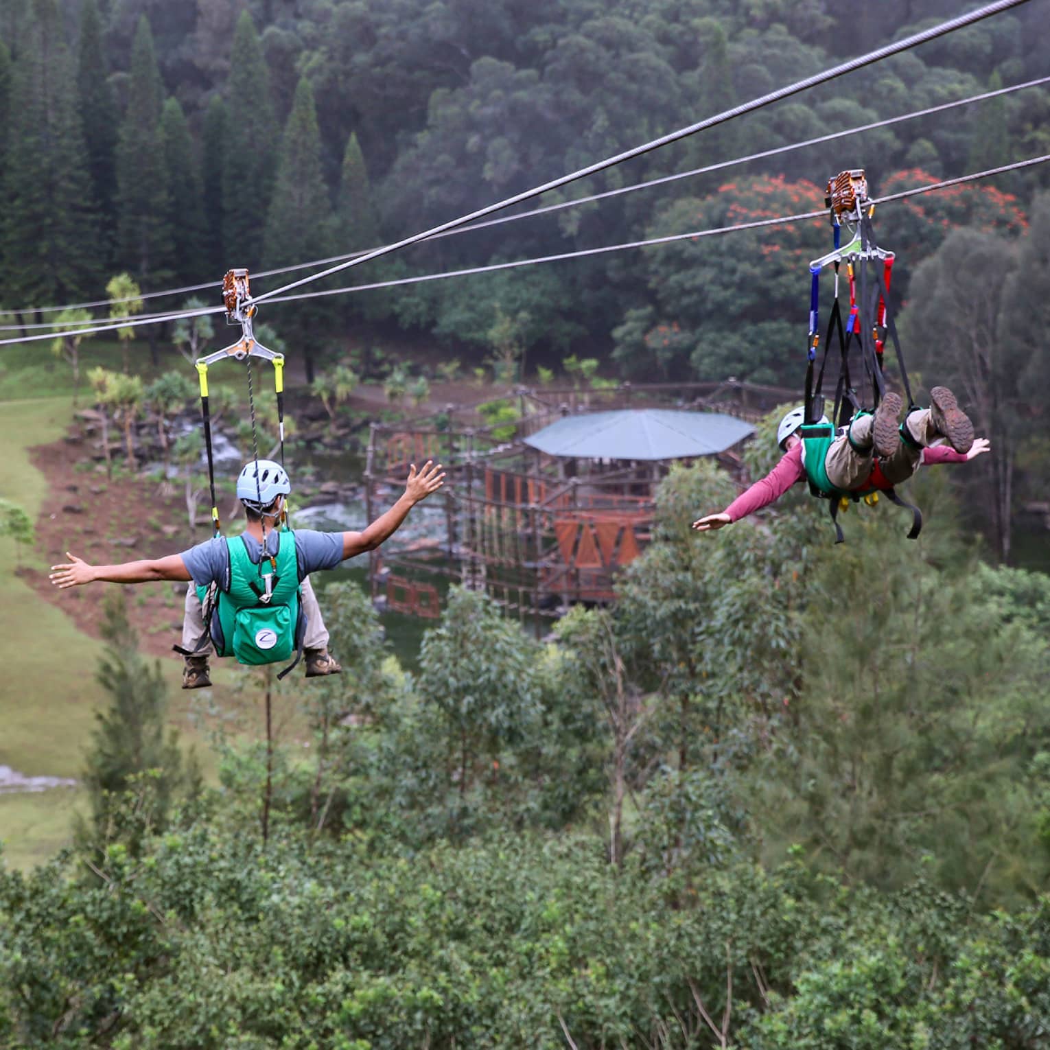 Adventure Park, two people glide down zip lines high above trees over mountain