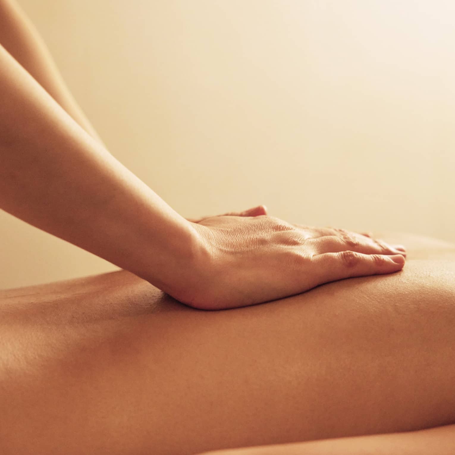 Masseuse rests hands on woman's bare back as she lays on massage table