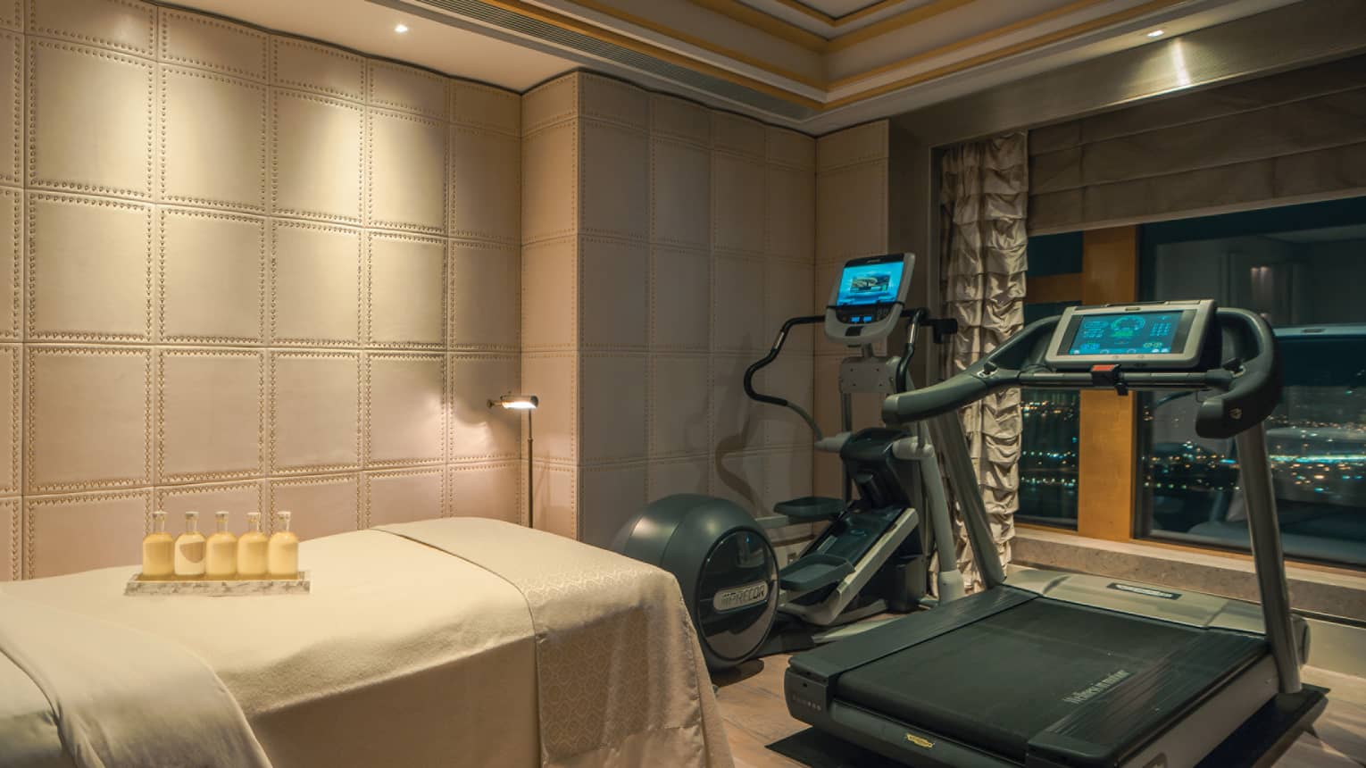 Private fitness room with a treadmill, elliptical machine, and massage table. Bottles of lotion are placed on the table.