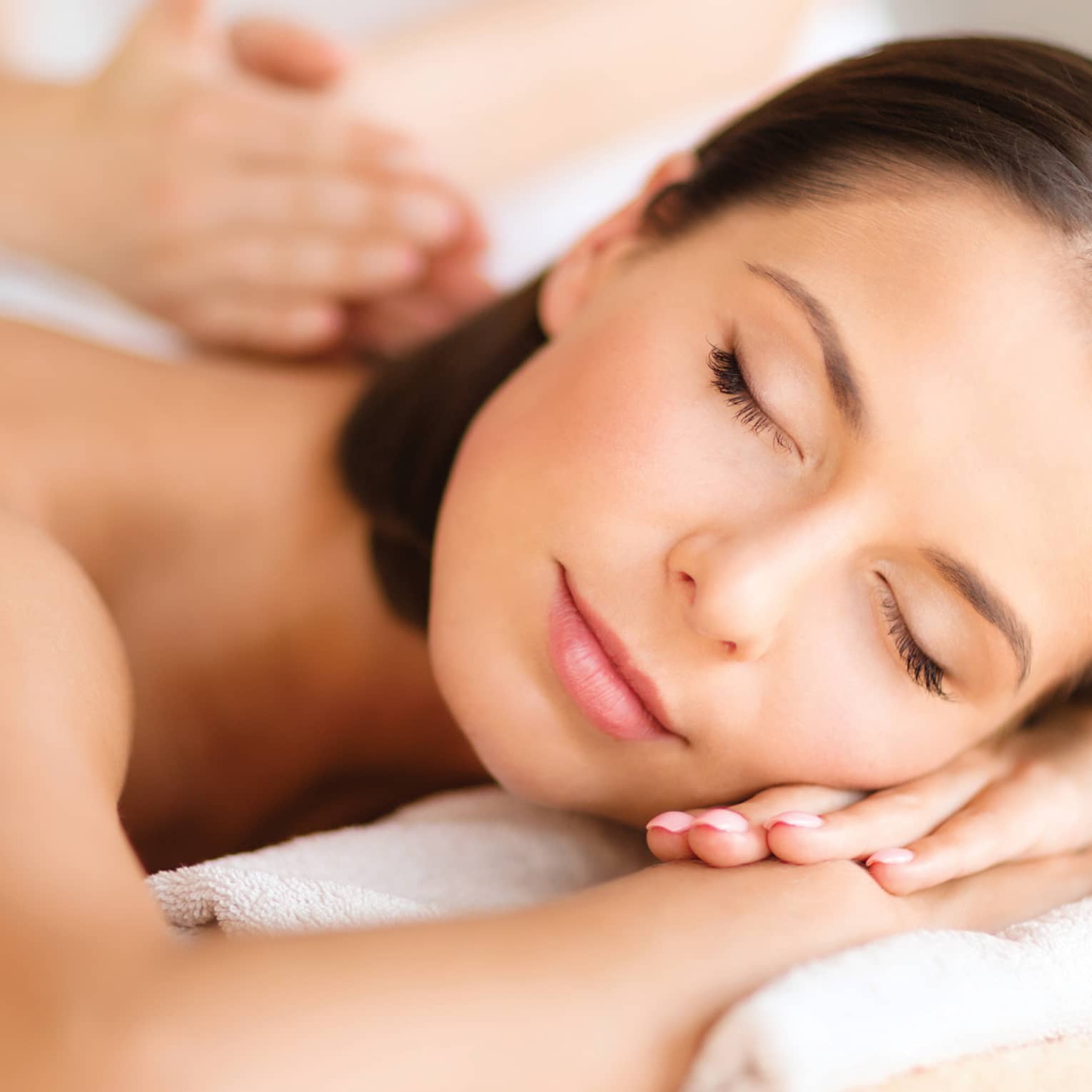 Woman lies on massage table, closes eyes. rests head on arms as spa staff massages back