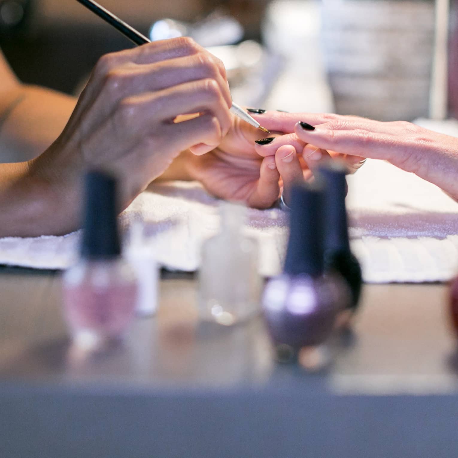 Close-up of spa staff painting woman's nails at manicure table