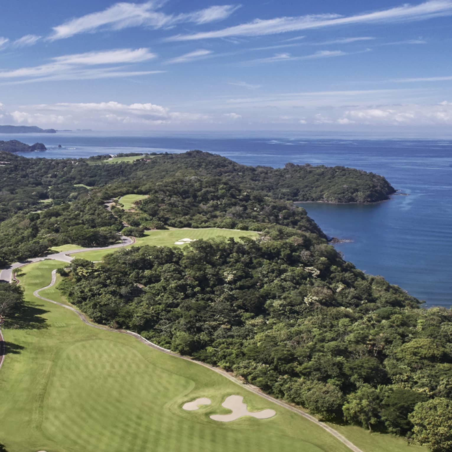Aerial view of a golf course that stretches along a verdant peninsula by the sea